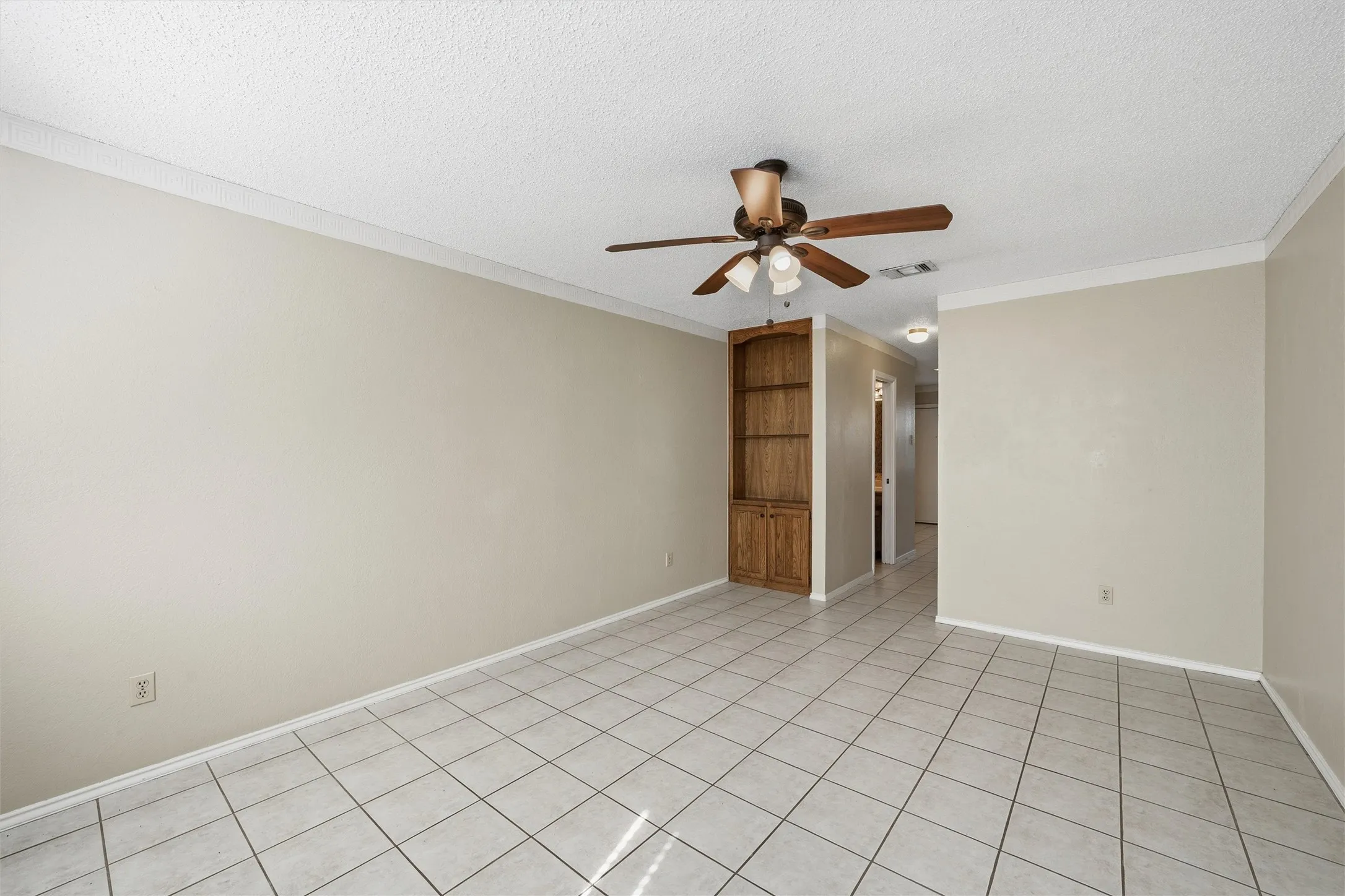 Neutral wall paint, crown molding, ceiling fan, built-in wooden shelving, and tile flooring