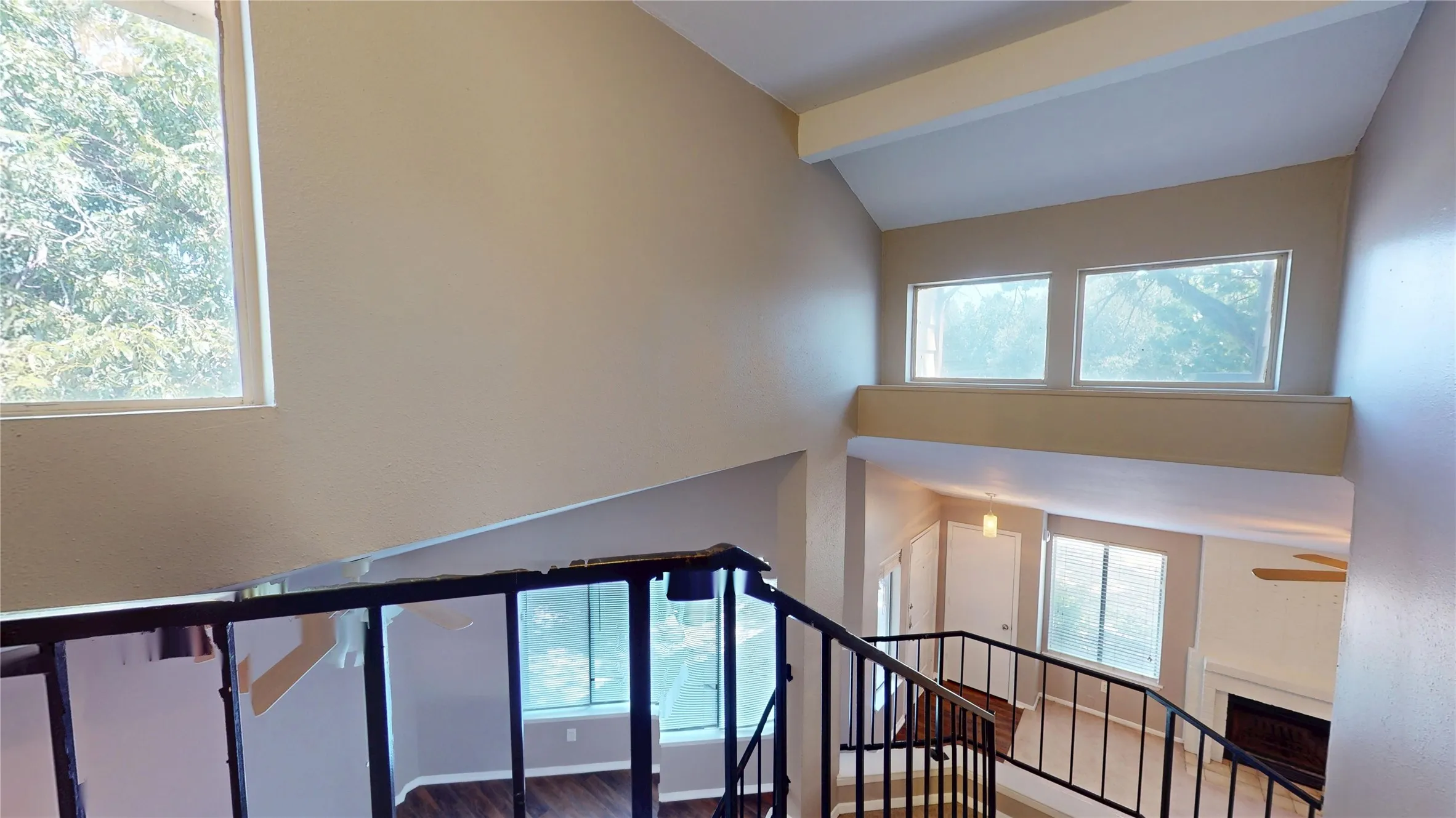 Vaulted ceilings with exposed beams, multiple windows, a wrought iron railing, and a fireplace