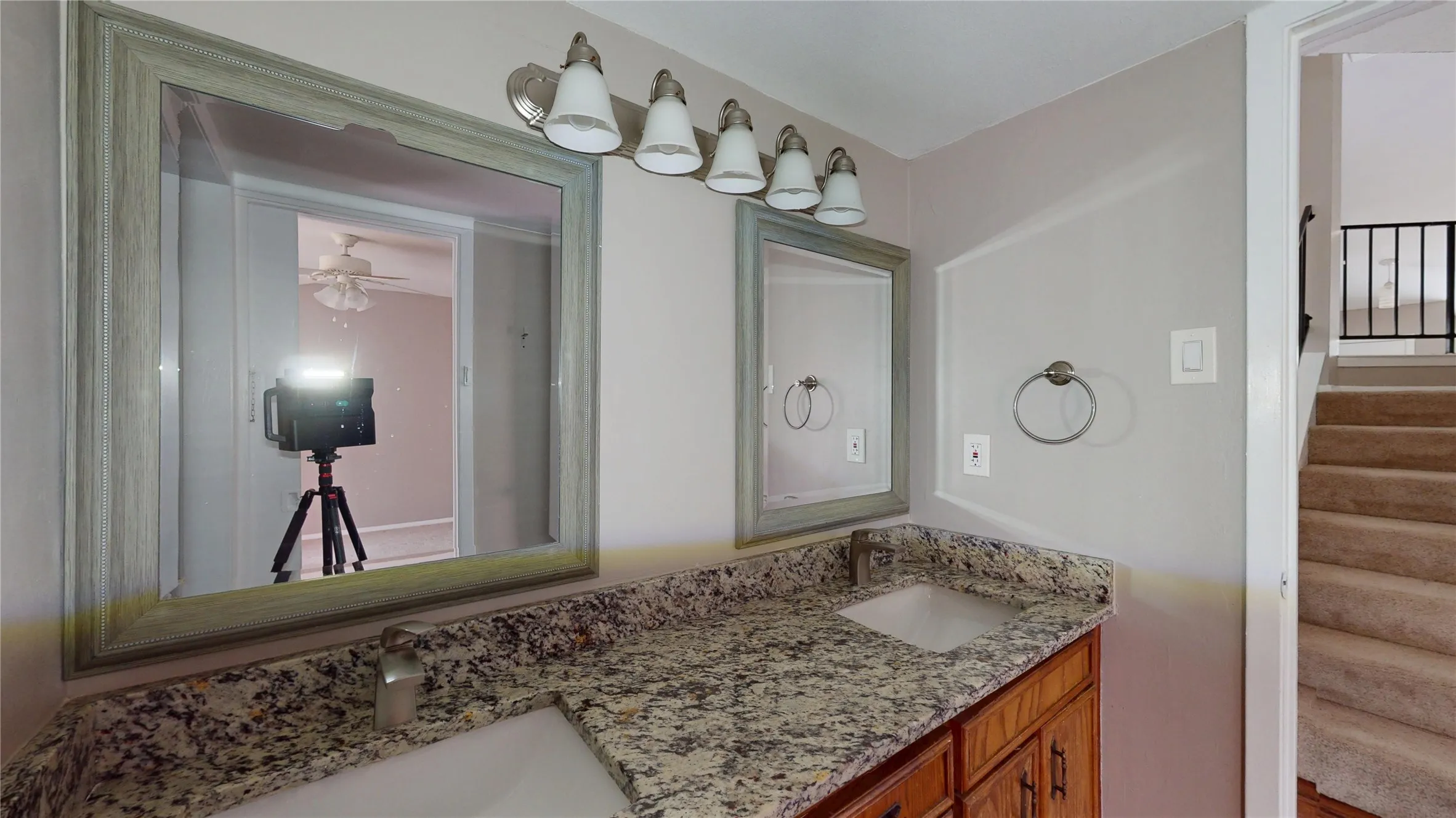 Dual vanity with granite countertop and integrated sinks, wood-finish cabinetry, and a multi-bulb light fixture