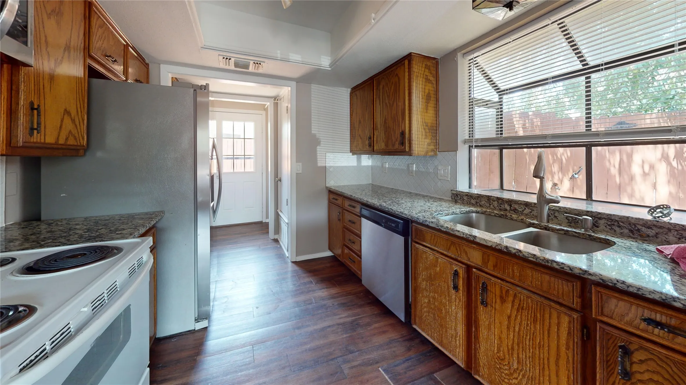 Kitchen featuring wood-finish cabinetry, stone countertops, a stainless steel double sink, and wood-finish flooring