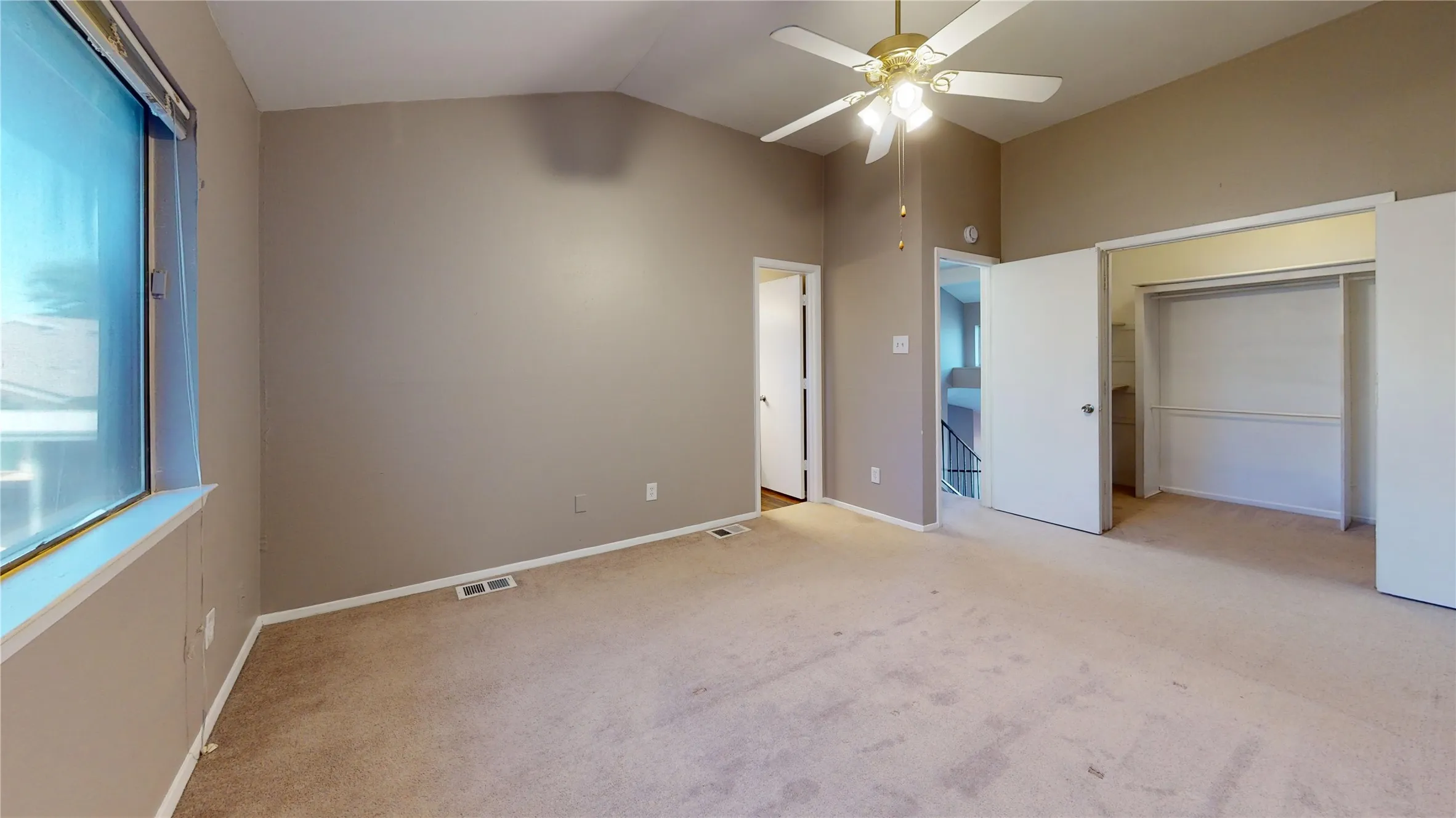 Vaulted ceiling, carpeted flooring, large window, ceiling fan with integrated lighting, and bi-fold closet doors