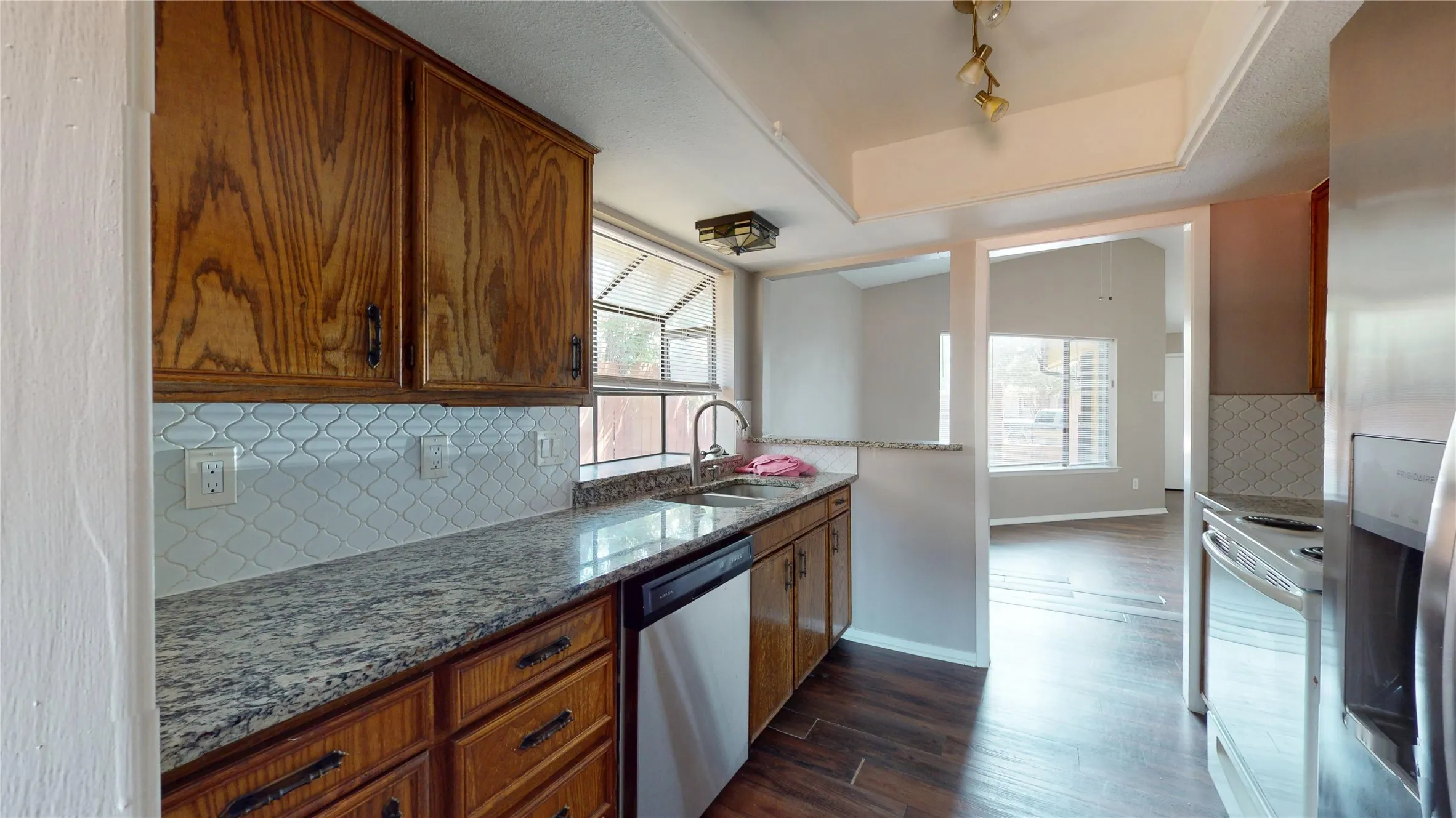 Kitchen featuring wood cabinetry, light-toned patterned backsplash, speckled countertops, stainless steel dishwasher, and wood-finish flooring