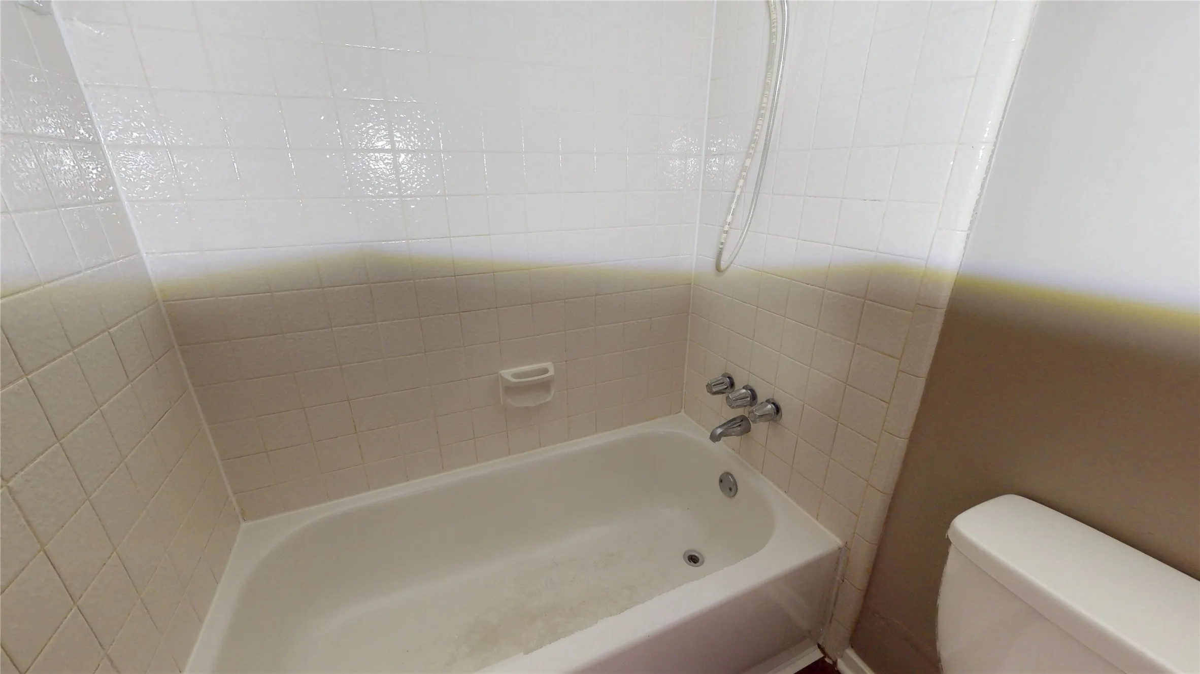 White tiled shower surround with a built-in soap dish, chrome fixtures, and a white bathtub