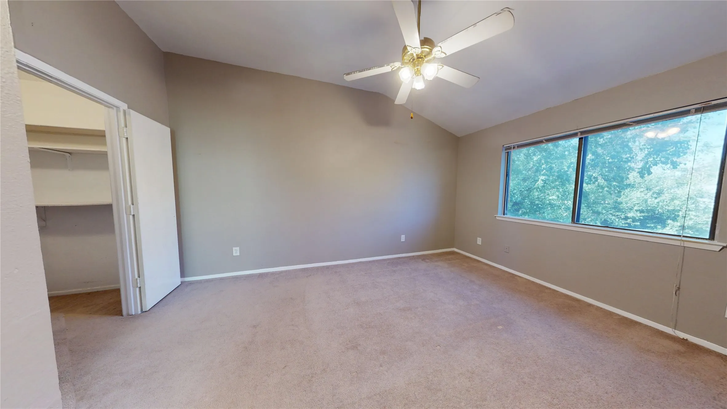 Vaulted ceiling room with large windows, wall-to-wall carpeting, and a ceiling fan