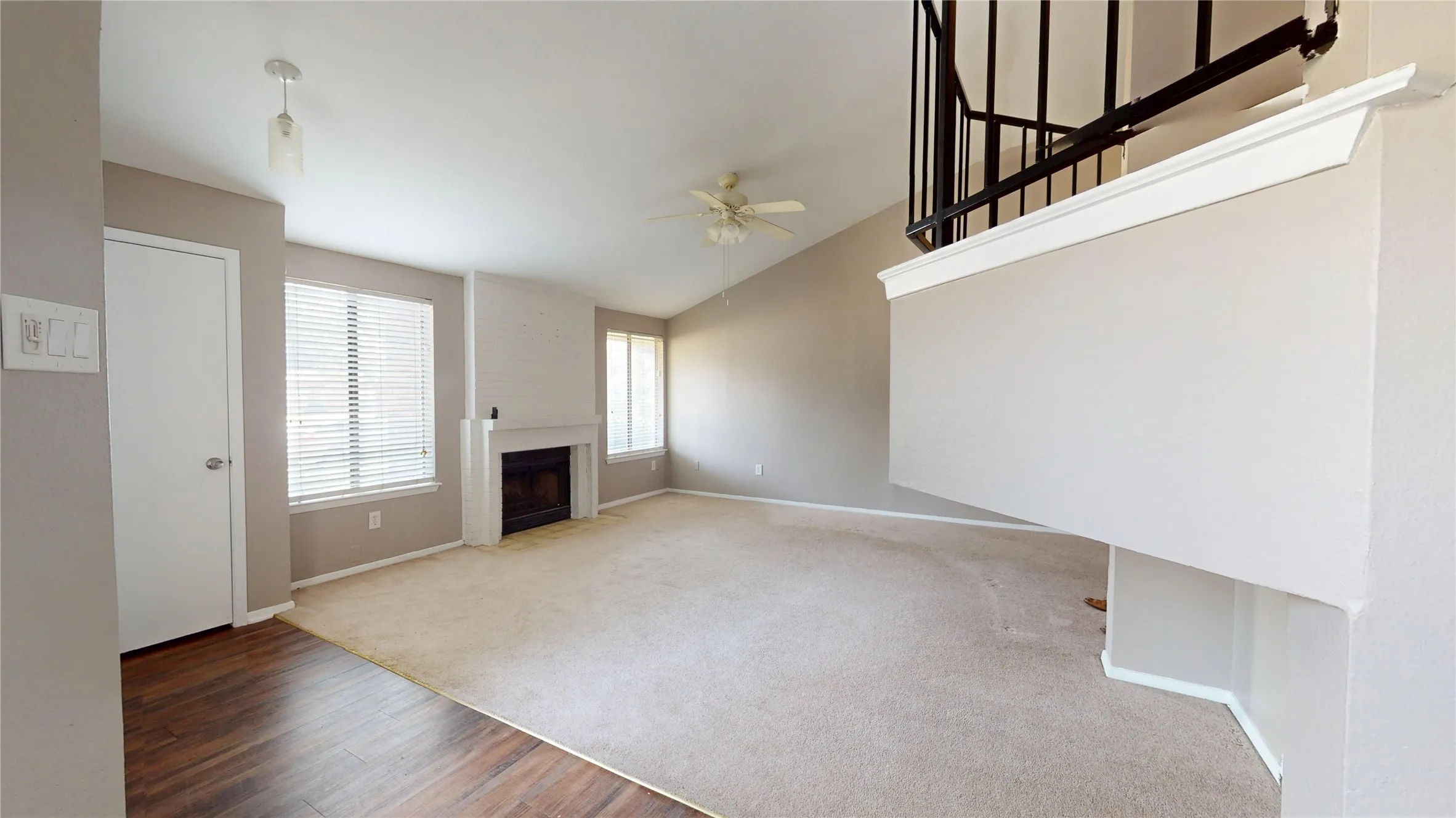 Vaulted ceiling with ceiling fan, white painted fireplace, wood-finish flooring, and a second-story railing