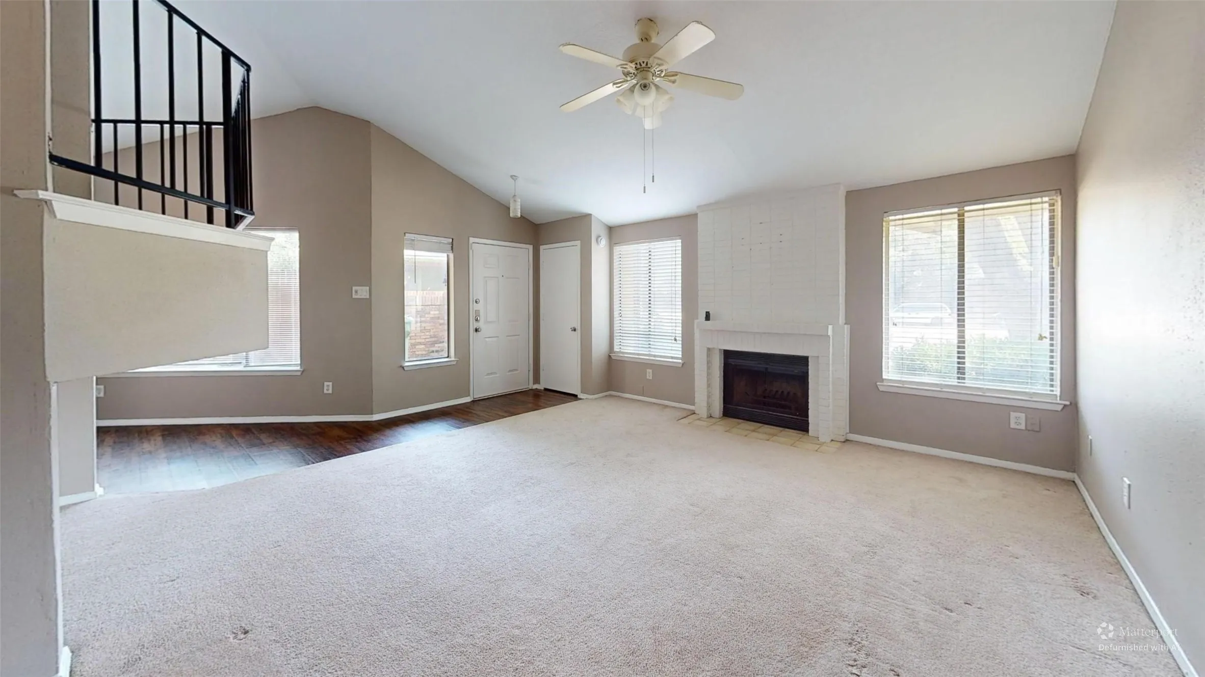 Vaulted ceiling with ceiling fan, white brick fireplace, multiple windows with blinds, and wood-finish flooring