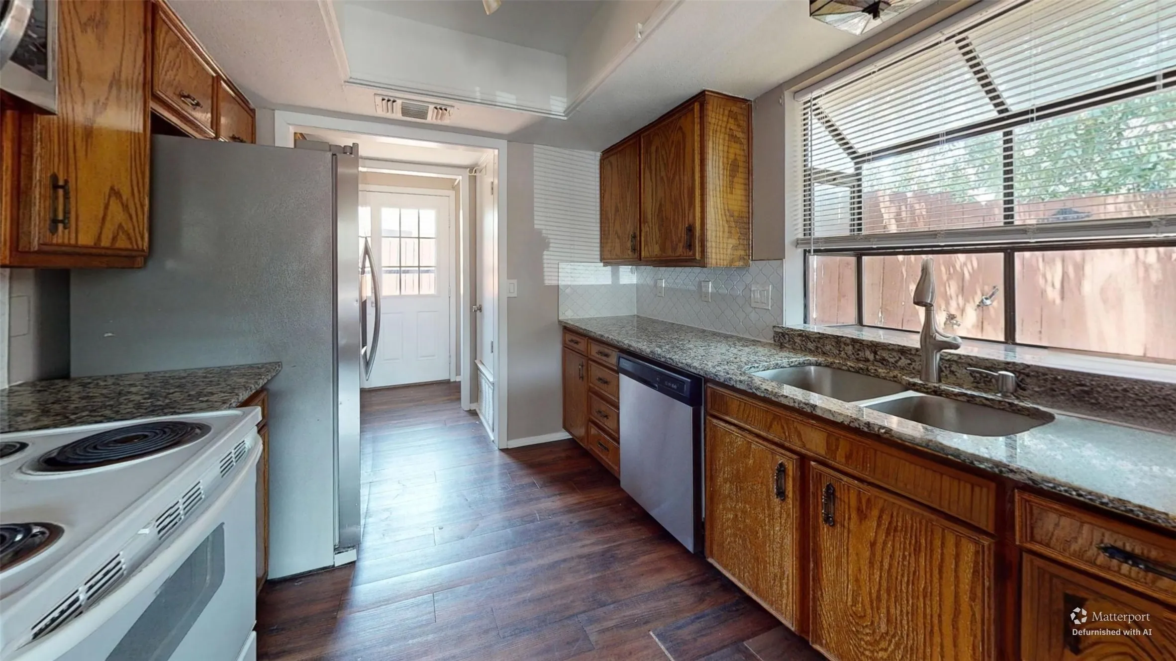 Kitchen featuring wood-finish flooring, granite-style countertops, wood cabinetry, a stainless steel refrigerator, and a double basin sink