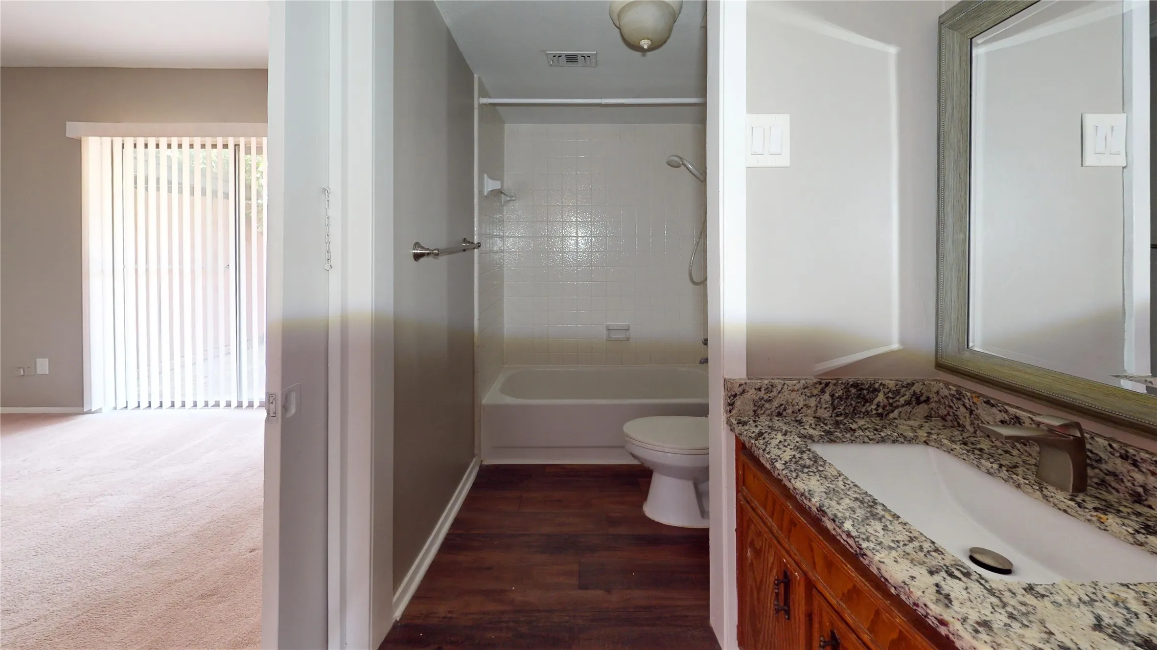 Vanity with stone countertop and integrated sink, framed mirror, and wood-finish flooring