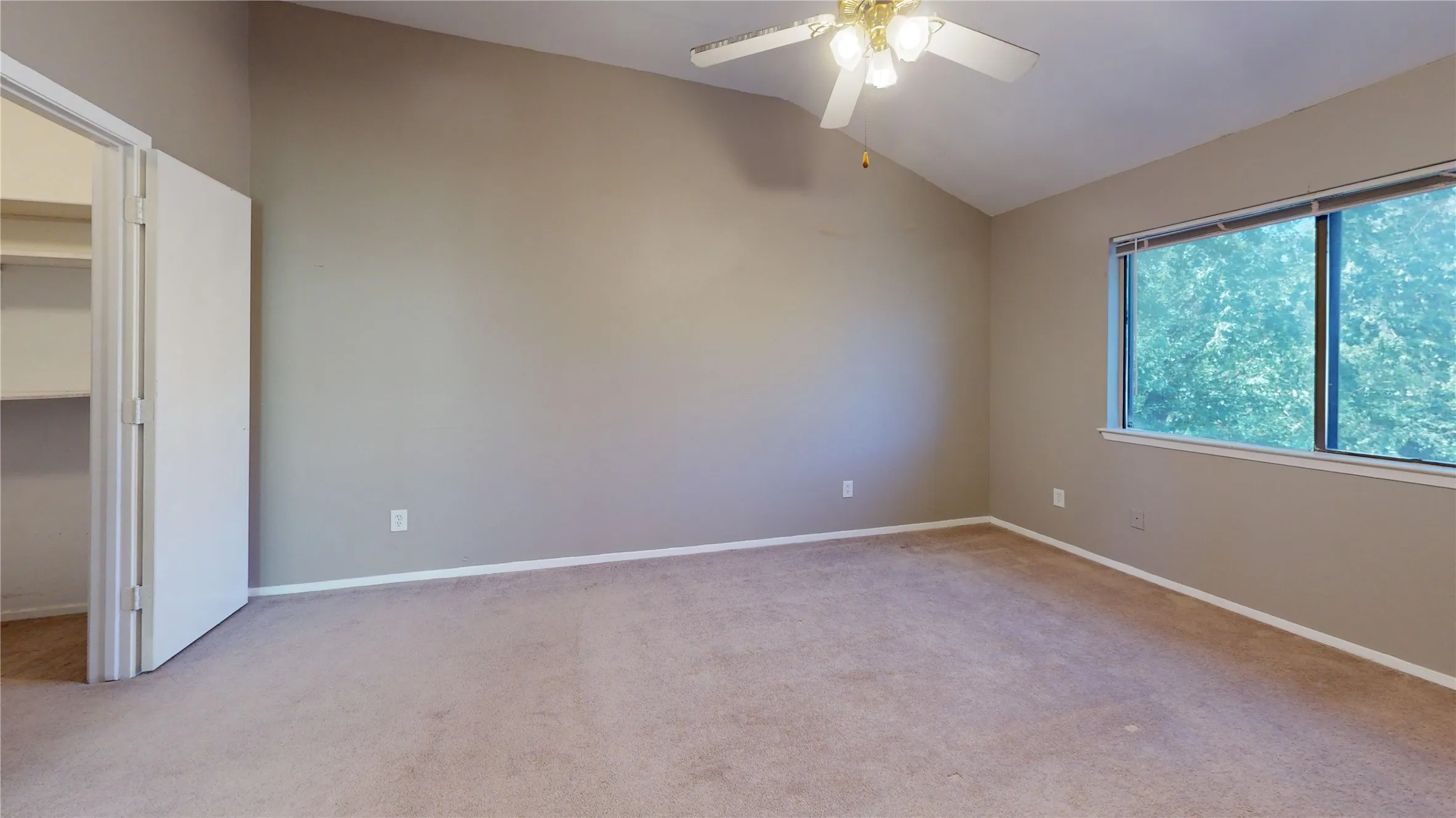 Vaulted ceiling, ceiling fan, large window, built-in closet shelving, and carpeting throughout