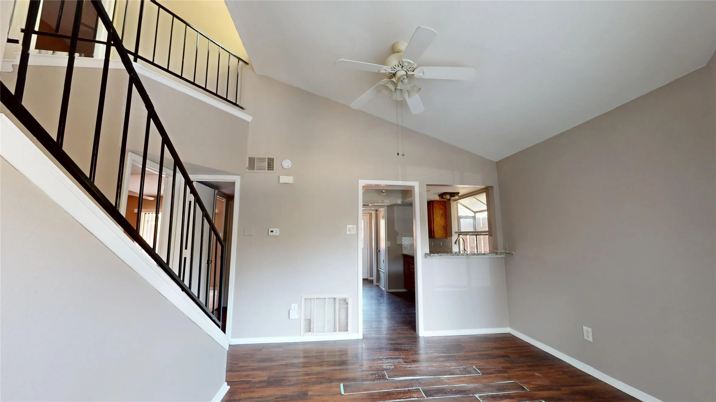 Vaulted ceiling with ceiling fan, wood-finish flooring, half-wall with countertop, and black metal stair railing