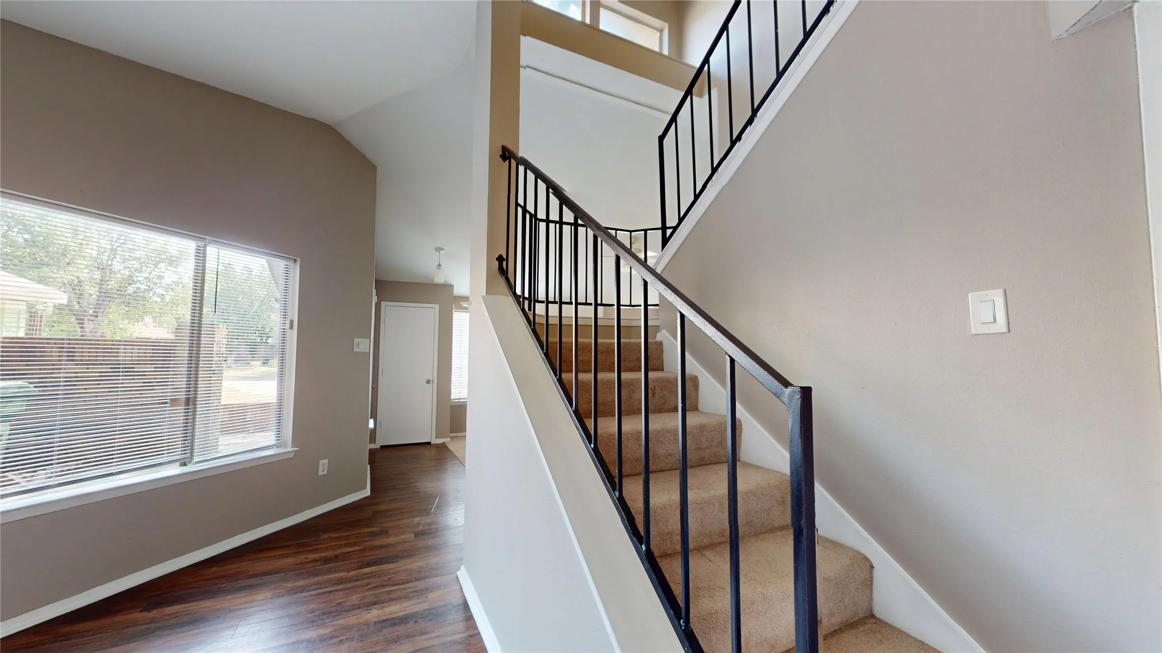 Vaulted ceilings, wood-finish flooring, two-story staircase with wrought iron railing, and carpeting on stairs