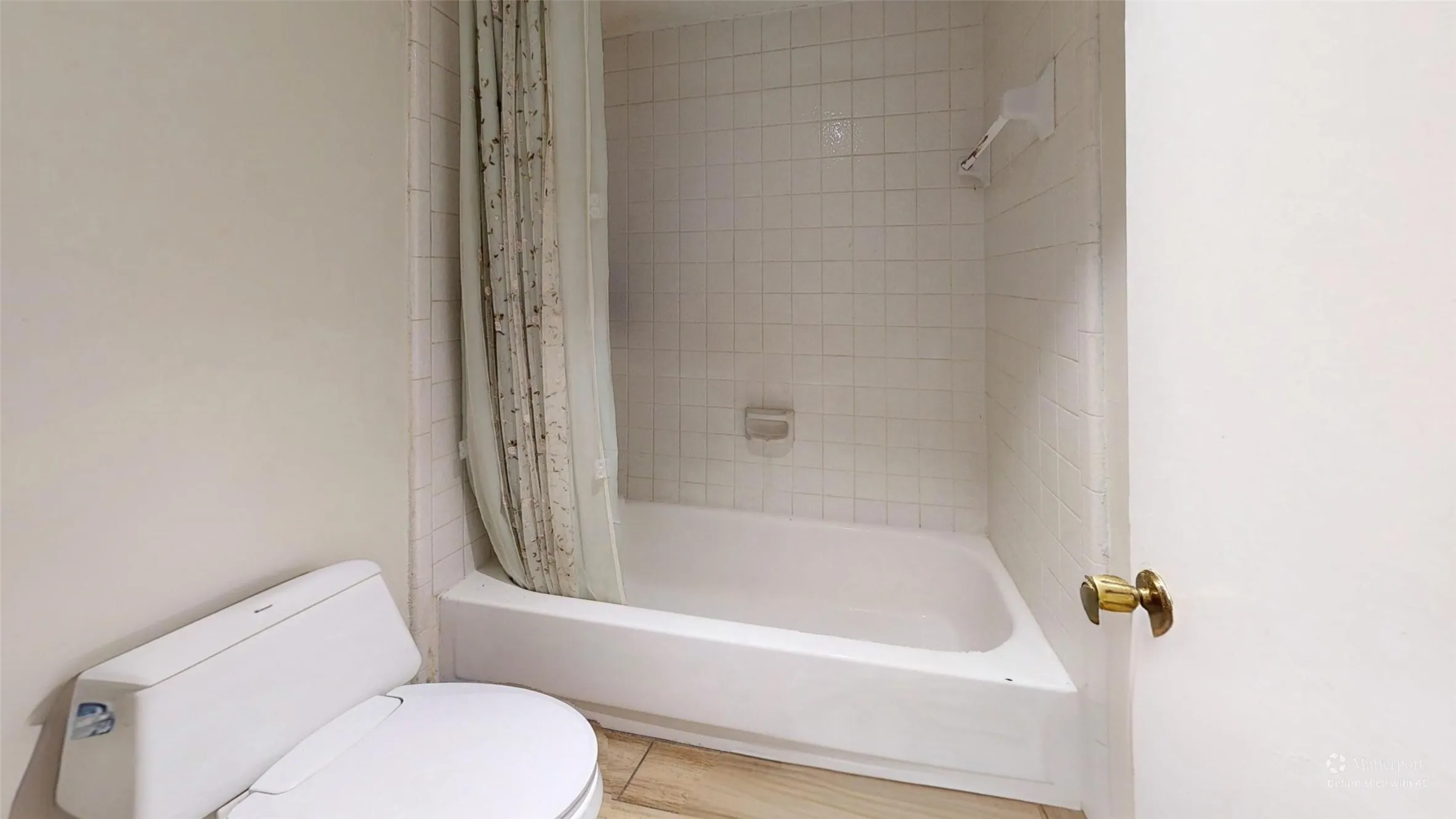 White ceramic toilet, white bathtub with a tiled surround, and wood-finish flooring