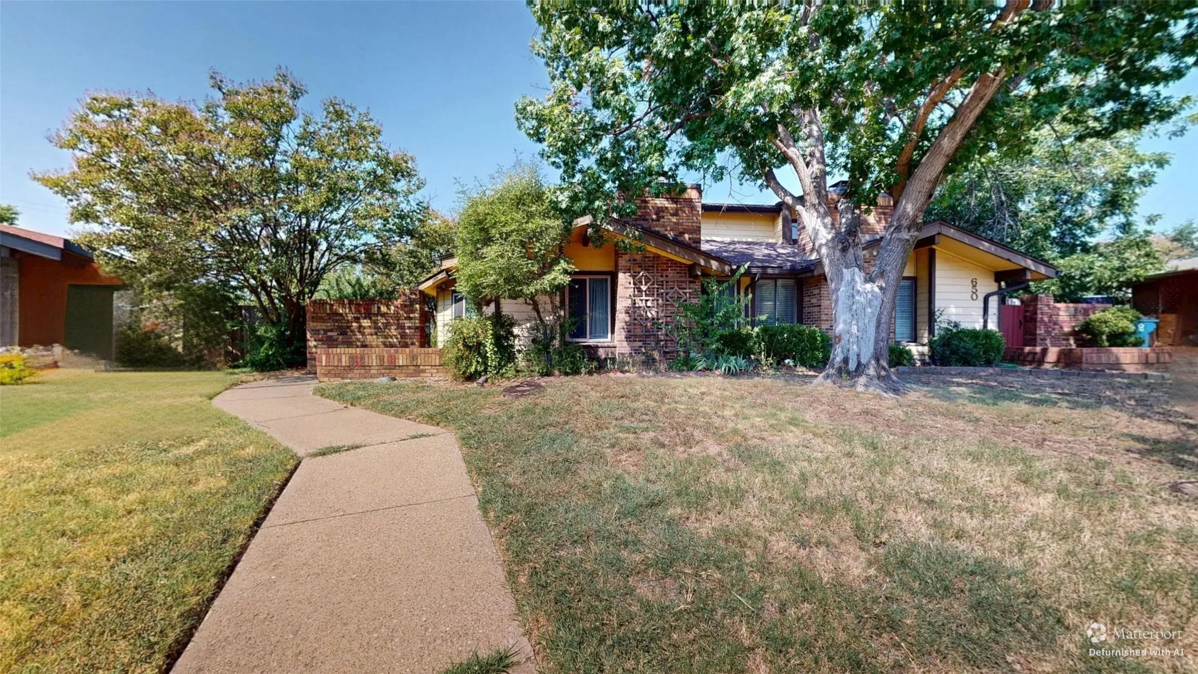 Brick exterior with siding accents, mature landscaping, paved walkway, and a prominent shade tree