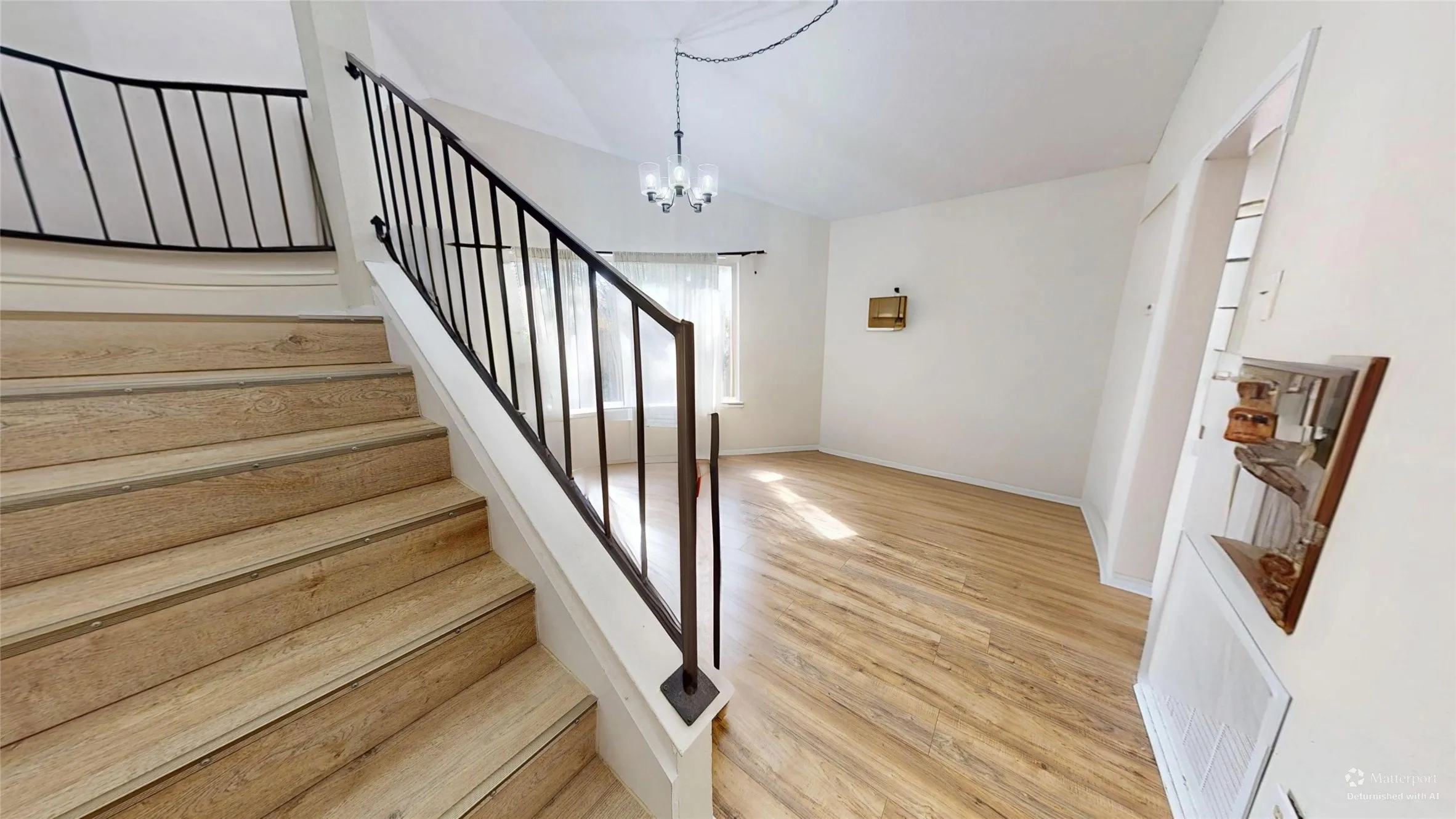 Wood-finish flooring, white walls, black metal staircase railing, vaulted ceiling, and a chandelier lighting fixture