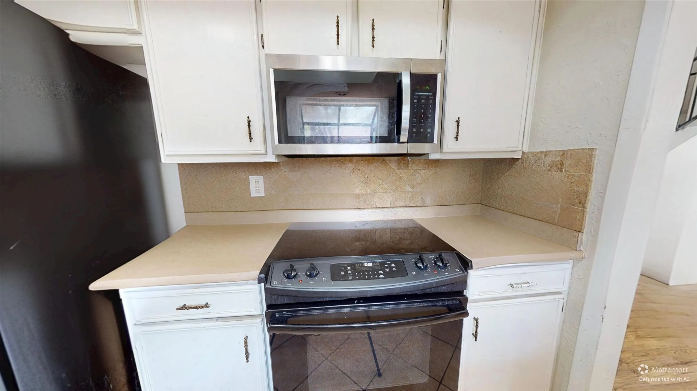 White cabinetry with dark hardware, stone-look countertops, stainless steel microwave, and a black electric range with an oven