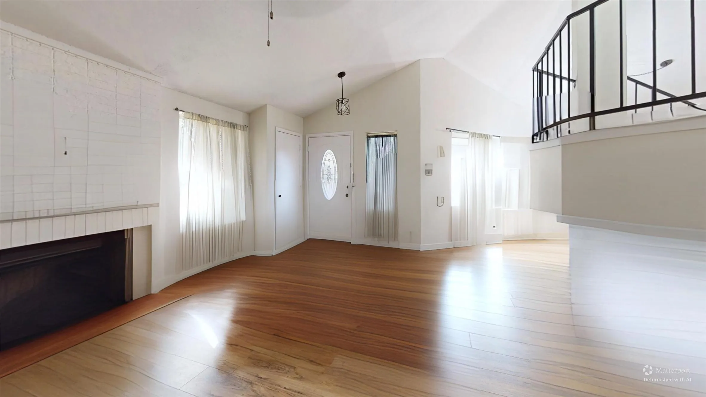 Wood-finish flooring throughout, featuring a fireplace with a tiled surround, vaulted ceilings, and a decorative interior railing