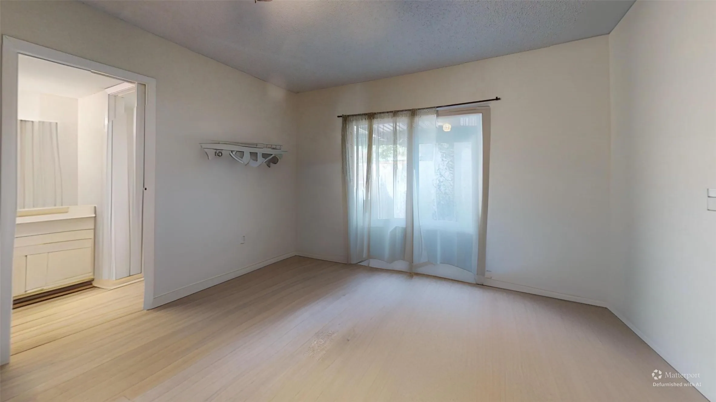 Light wood-finish flooring throughout, bright white walls, and a sliding glass door providing natural illumination