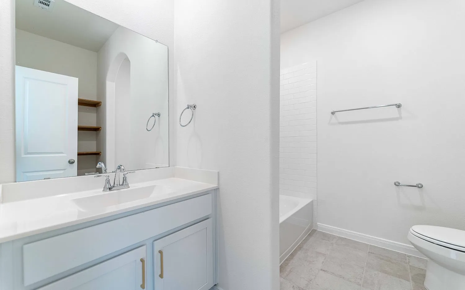 White vanity with a single basin sink, wall-mounted mirror, built-in shelving, white subway tile shower surround, and gray tile flooring