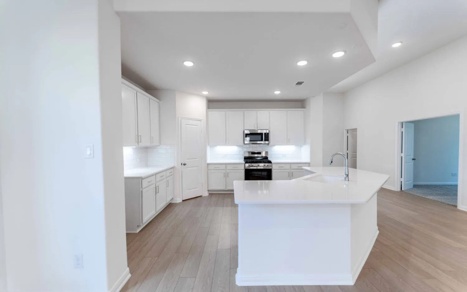 Modern kitchen featuring white cabinetry, stainless steel appliances, white quartz countertops, a large center island with waterfall edge, and wood-finish flooring throughout the open-concept space