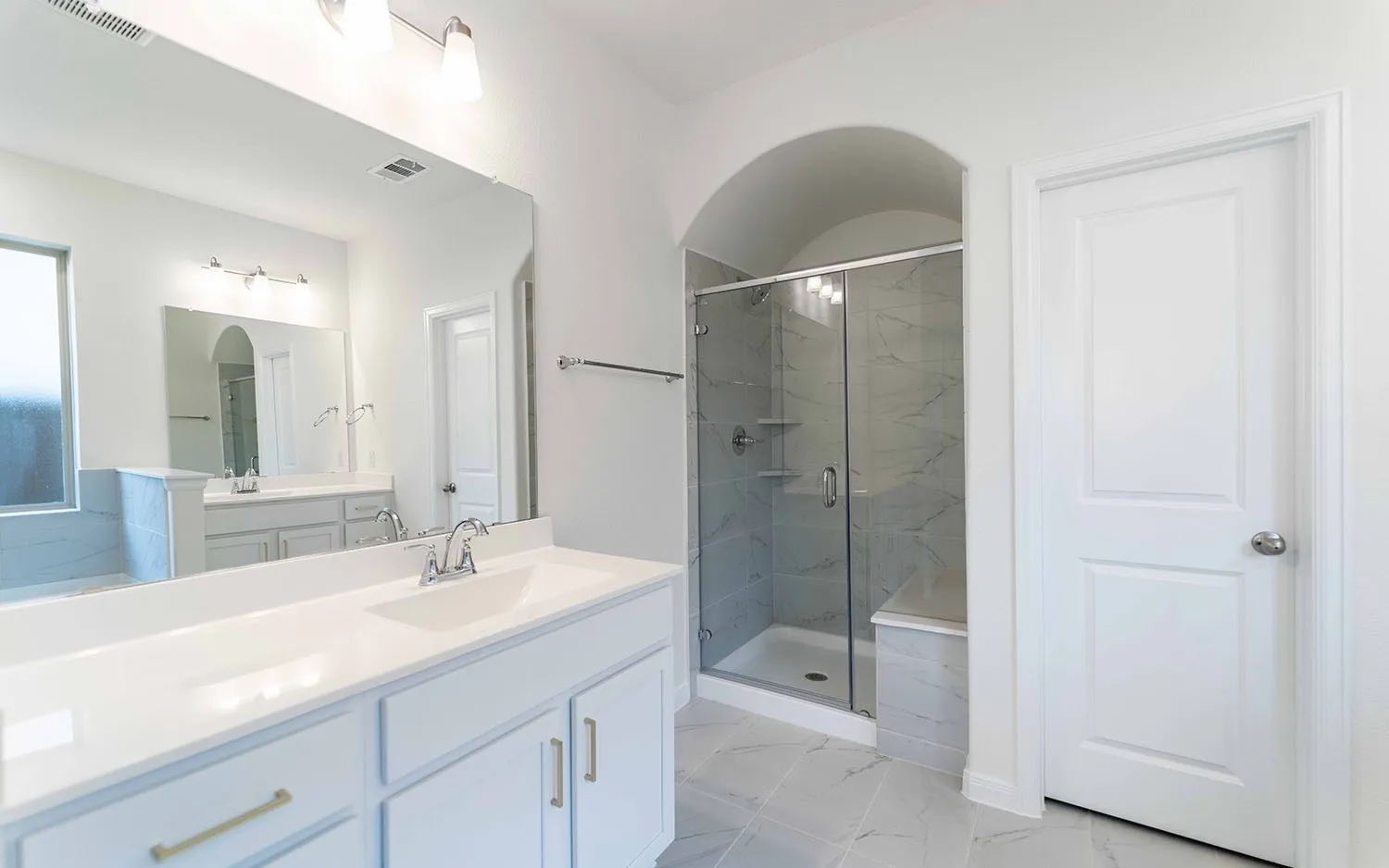 Double vanity with white cabinetry, gold-finish hardware, and a large mirror