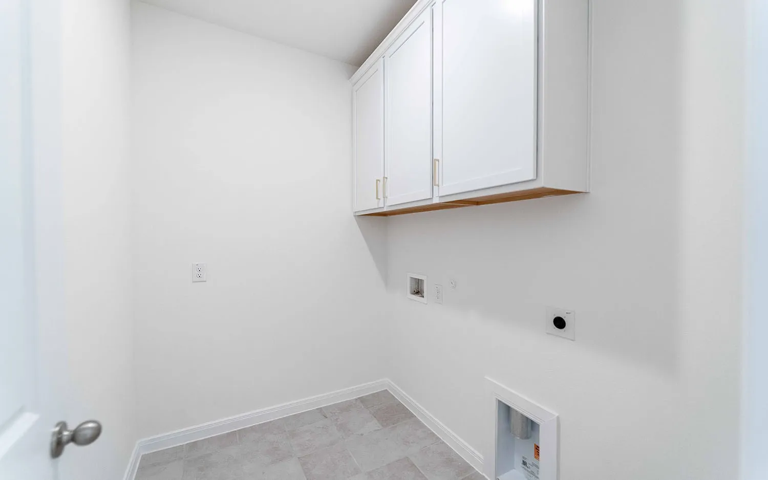 Utility room featuring white cabinetry with wood-finish trim, tile flooring, electrical outlet, and built-in storage for laundry and household essentials