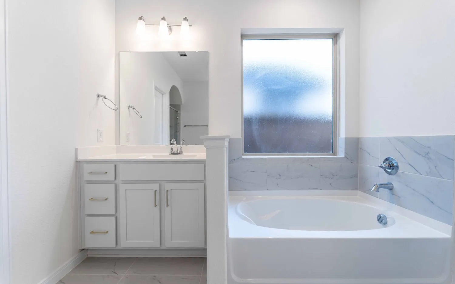 Built-in bathtub with a tiled surround, single vanity with a solid surface countertop, and large mirror with overhead lighting
