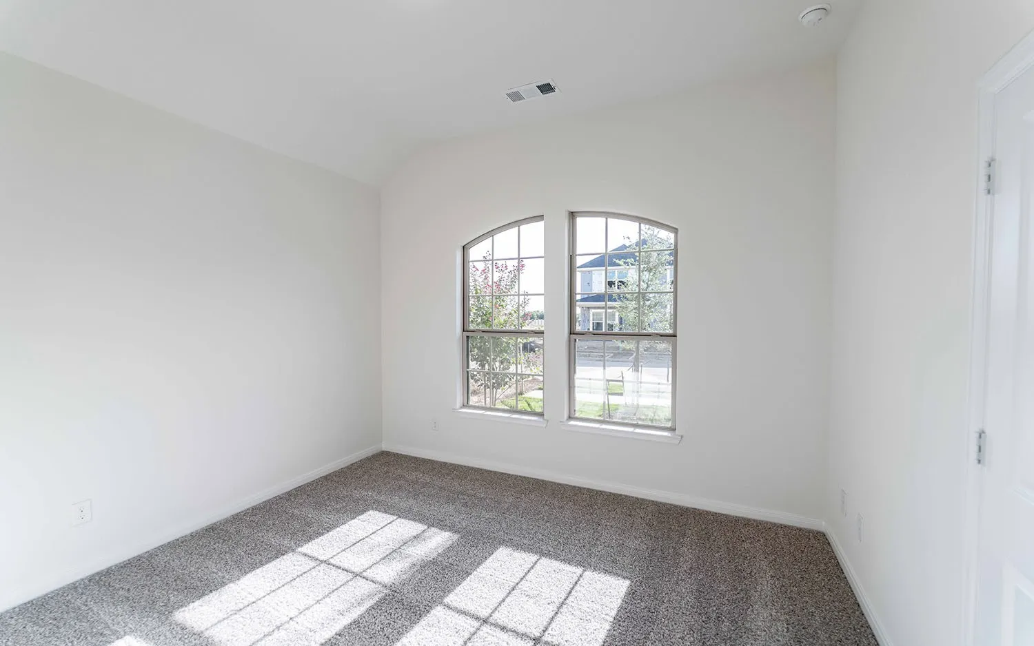 Arched window with gridded panes, light-toned carpet flooring, white painted walls, and a white interior door