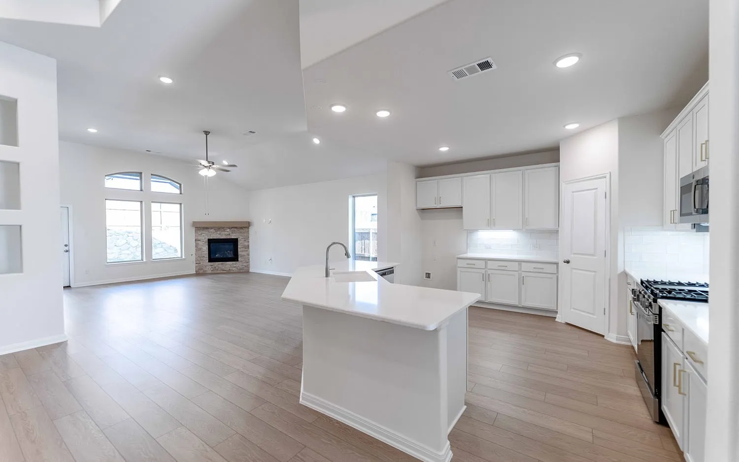 Open-concept living space featuring wood-finish flooring, a stone-surround fireplace with a wood mantle, and an arched window