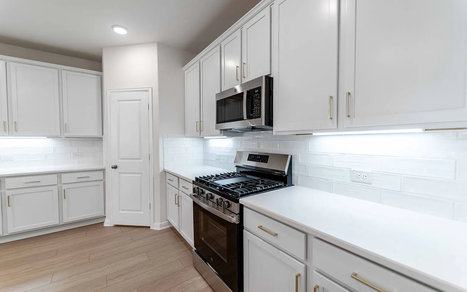 Modern kitchen featuring white shaker-style cabinetry with brushed nickel hardware, white subway tile backsplash, stainless steel gas range with convection oven, integrated microwave, and white quartz countertops
