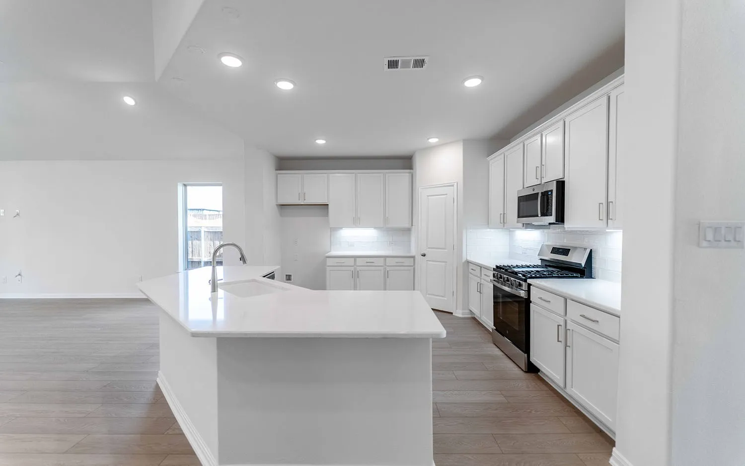 Kitchen with white cabinetry, stainless steel appliances, a white tile backsplash, and a center island with an integrated sink