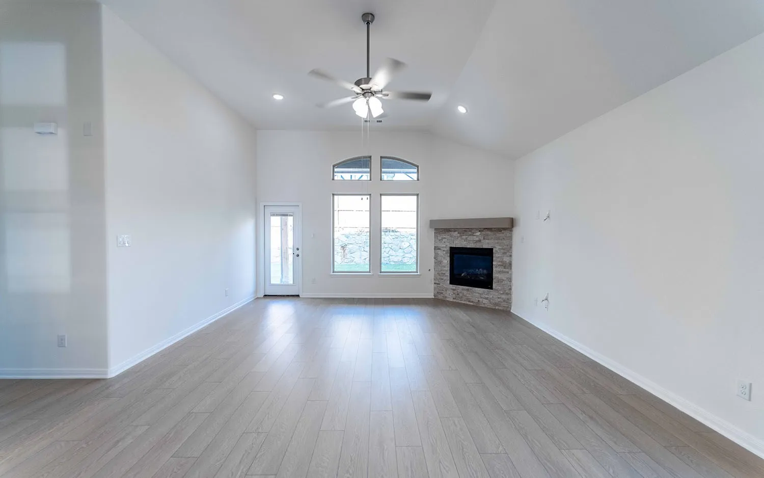 Vaulted ceilings with recessed lighting, wood-finish flooring, and a contemporary fireplace with a stone surround and wood mantel