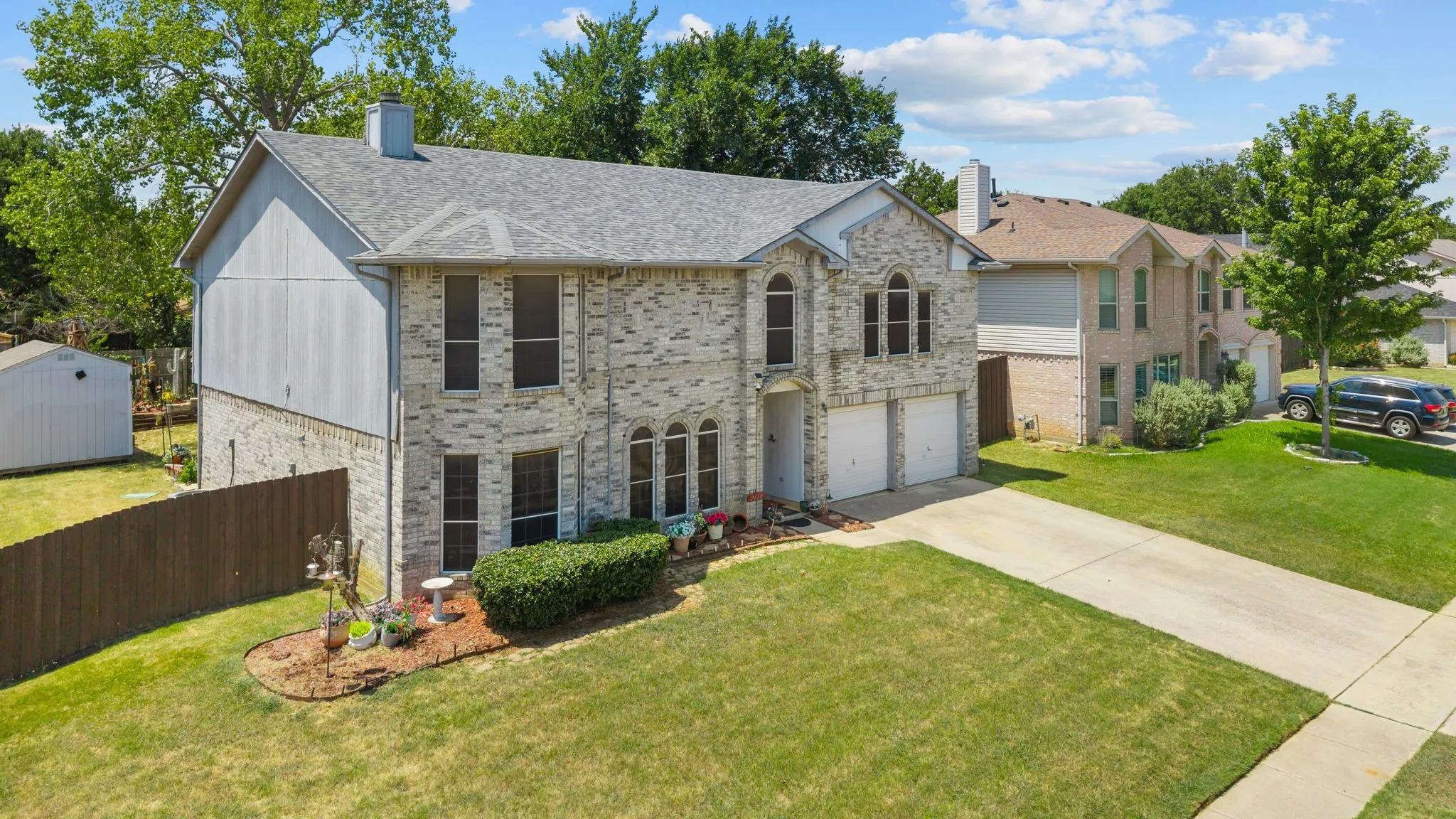 Brick exterior with an attached two-car garage, mature landscaping, and a fenced backyard