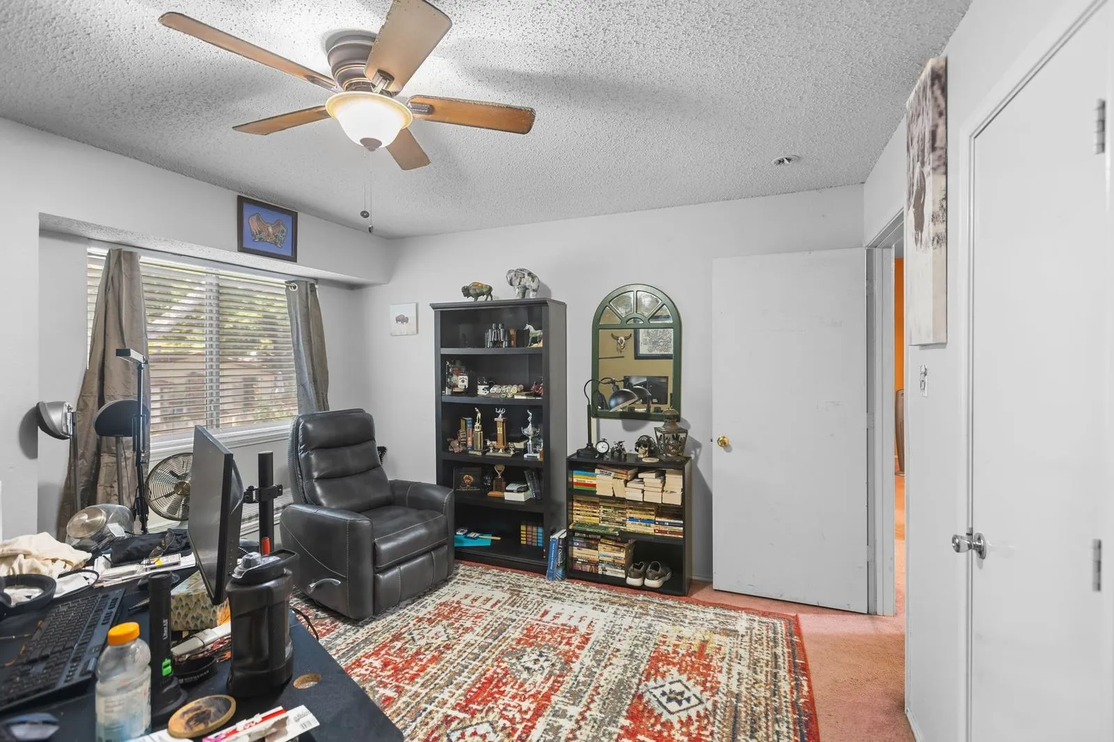 Ceiling fan with integrated lighting, window with blinds, built-in shelving, white paneled door, and neutral-colored walls