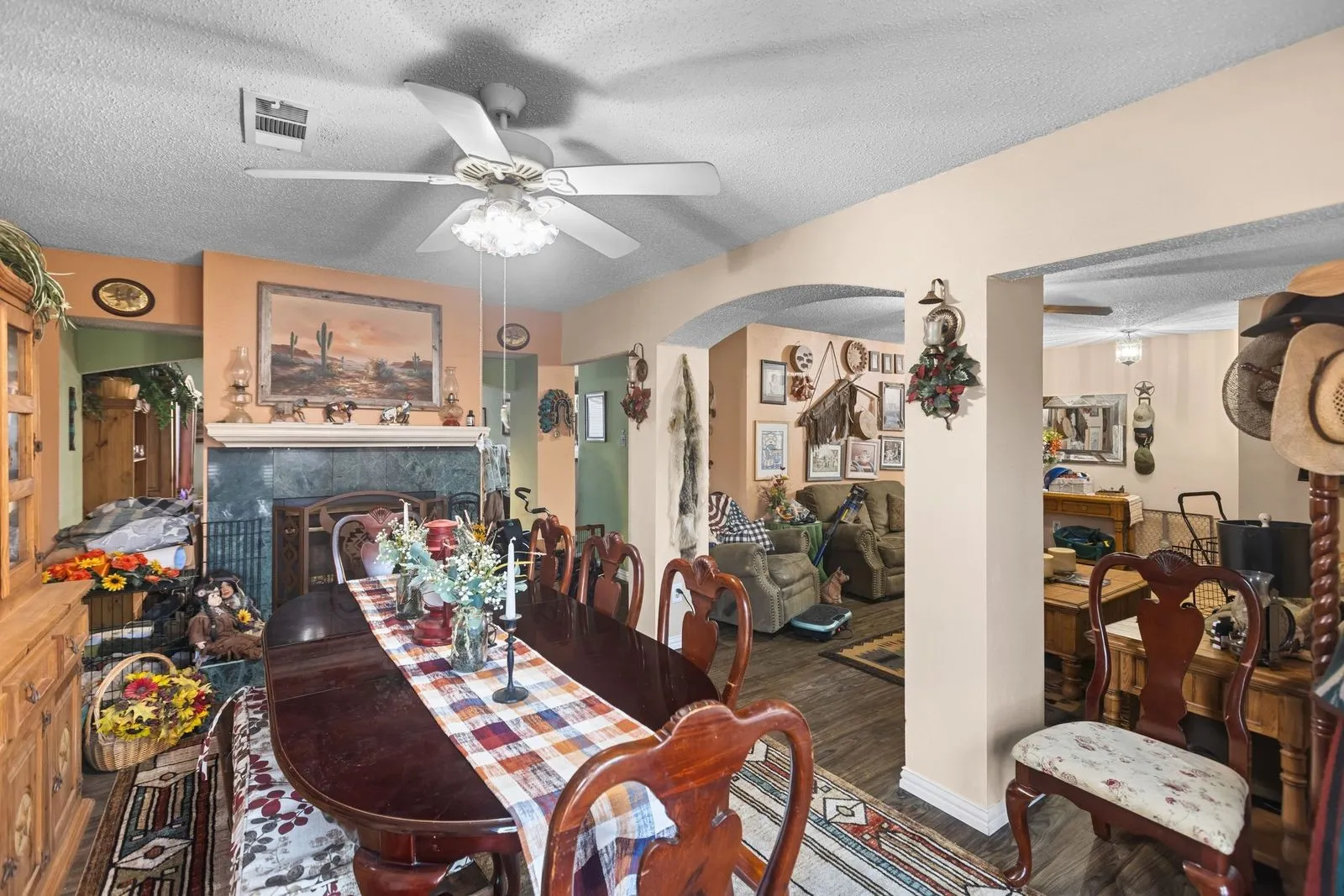Wood-finish flooring throughout, a ceiling fan with integrated lighting, and a fireplace with a stone surround