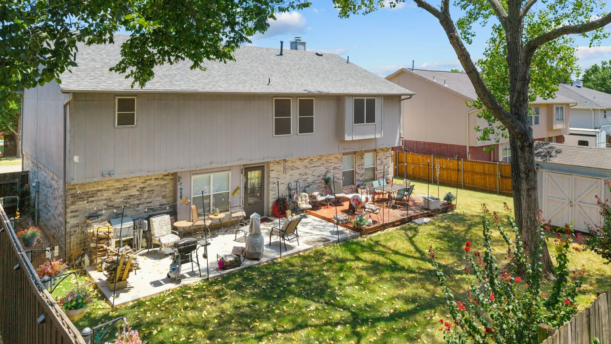 Expansive backyard featuring a manicured lawn, a concrete patio, a wooden deck, and a storage shed