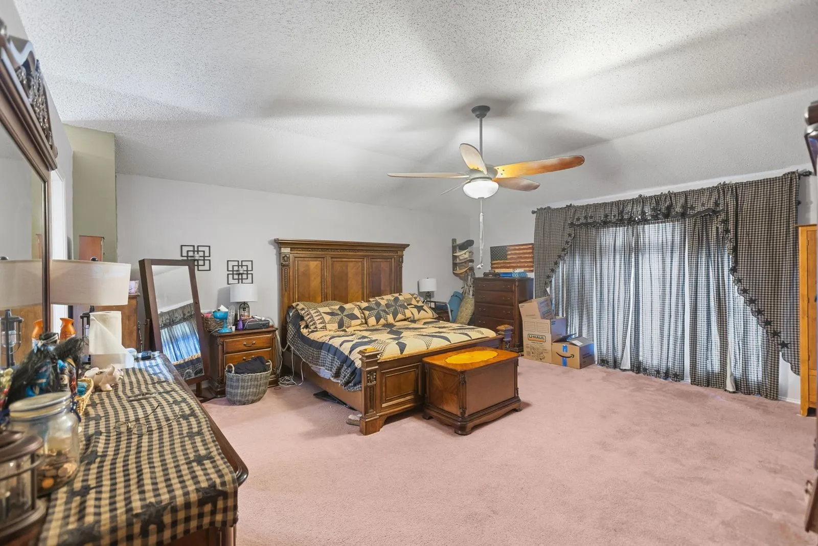 Sloped ceiling with a ceiling fan, carpeted flooring, and a large window with privacy coverings