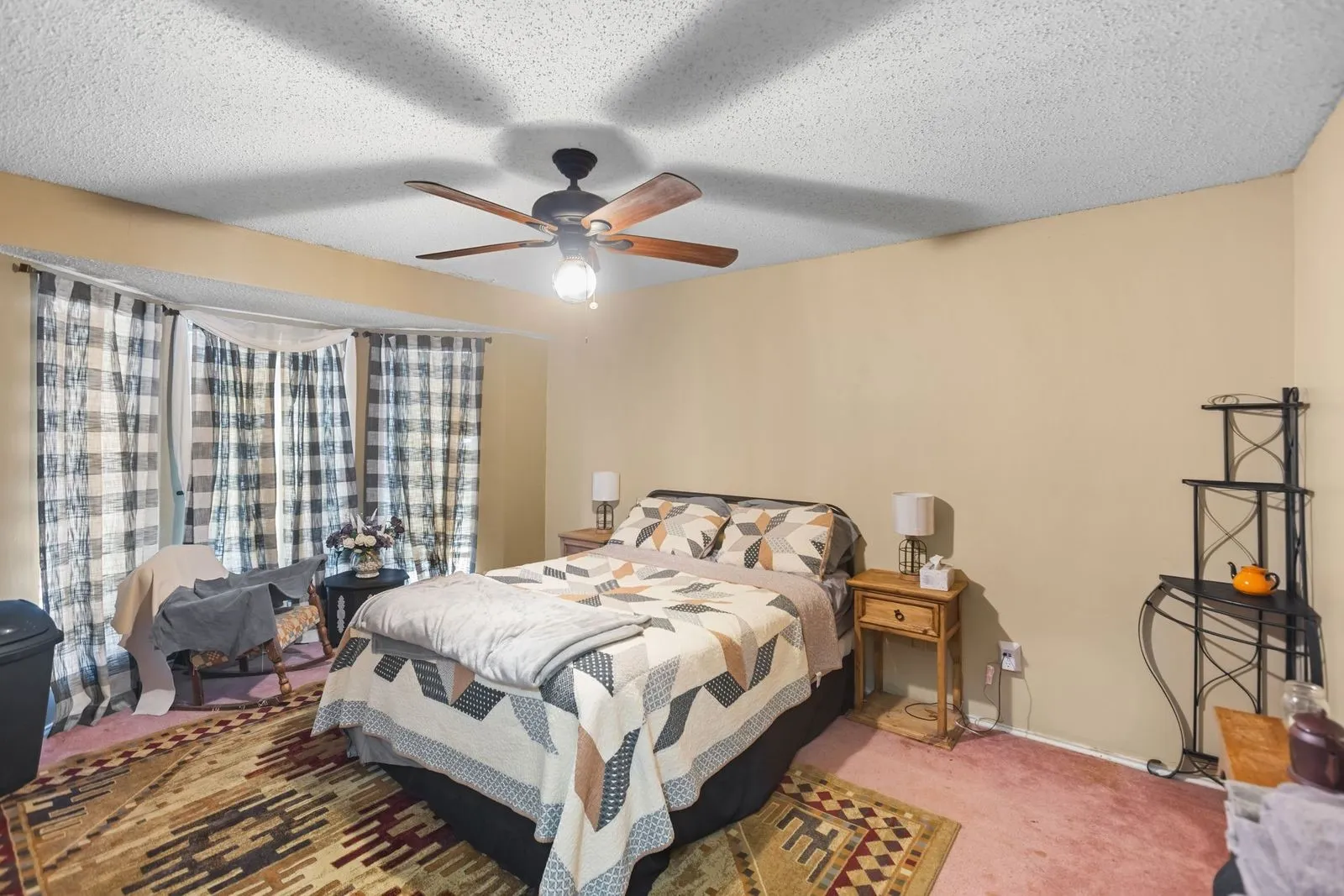 Bay window with multiple panels, textured ceiling, ceiling fan with wood-finish blades, soft-toned wall paint, and wall-to-wall carpeting