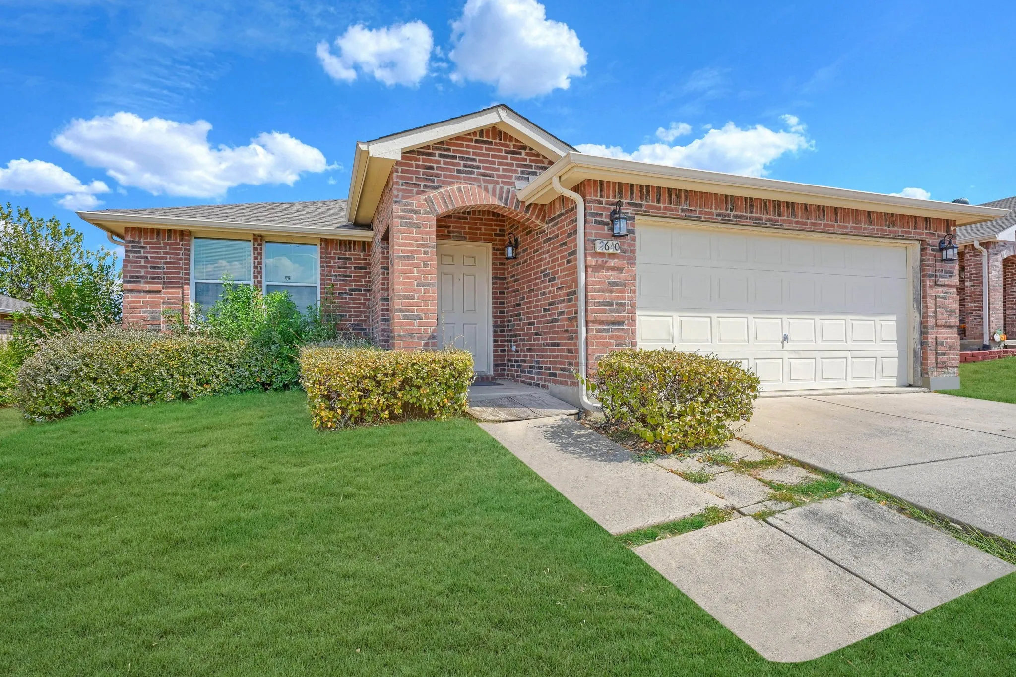 Brick exterior with an arched entry, two-car garage, concrete driveway, and a manicured lawn