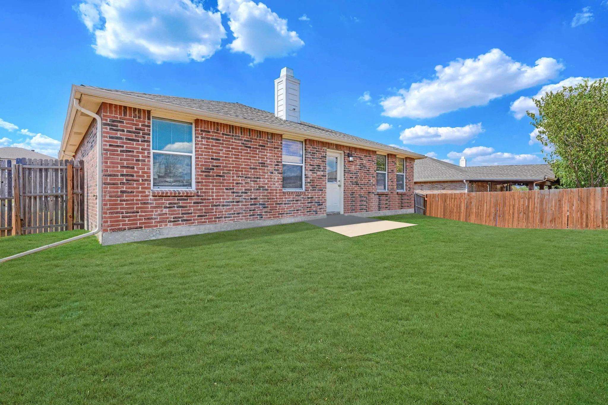 Spacious grass lawn, full brick exterior, chimney feature, privacy fencing, and concrete patio