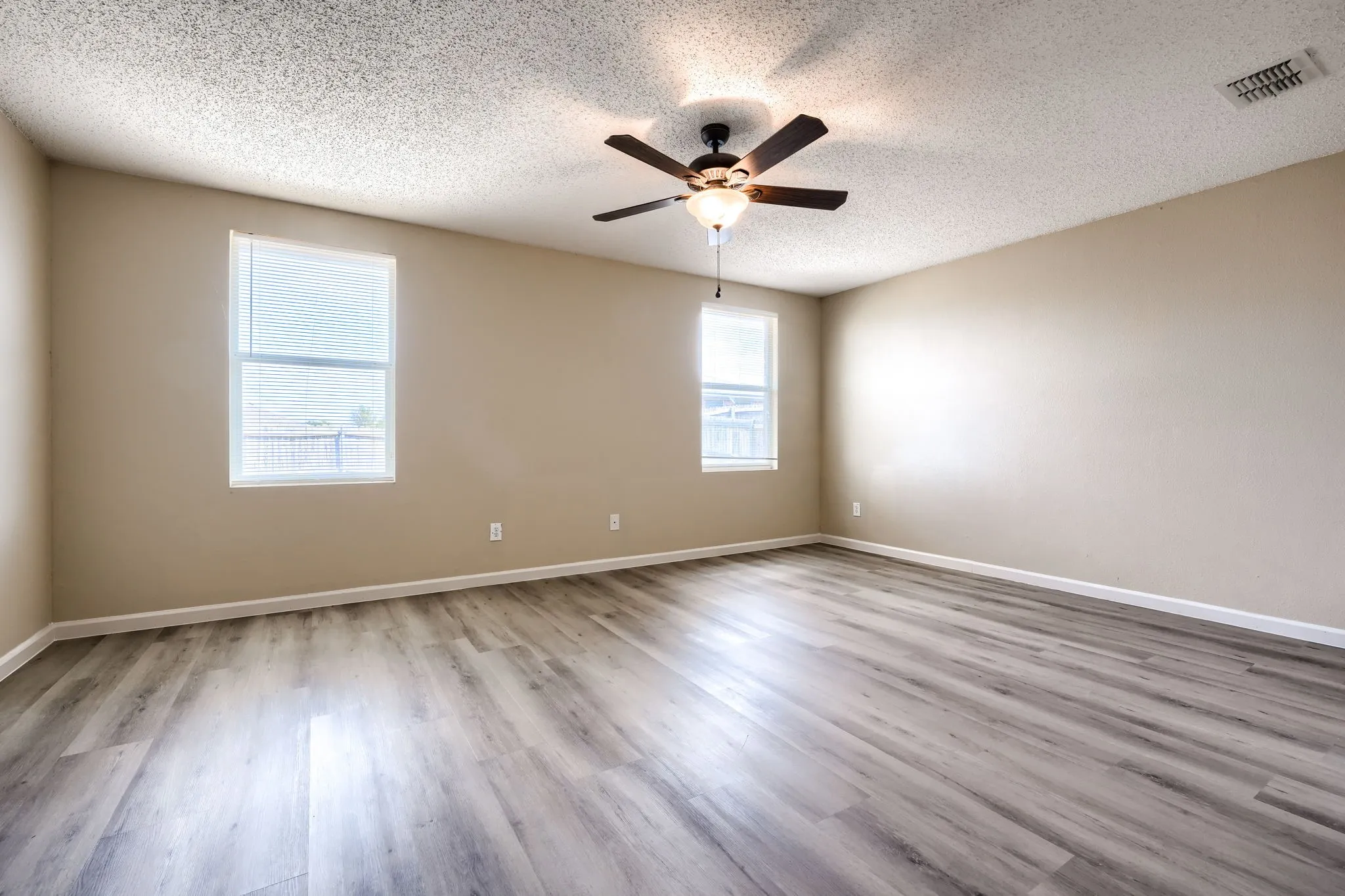Spacious room featuring wood-finish flooring, neutral-toned walls, and a ceiling fan with integrated lighting