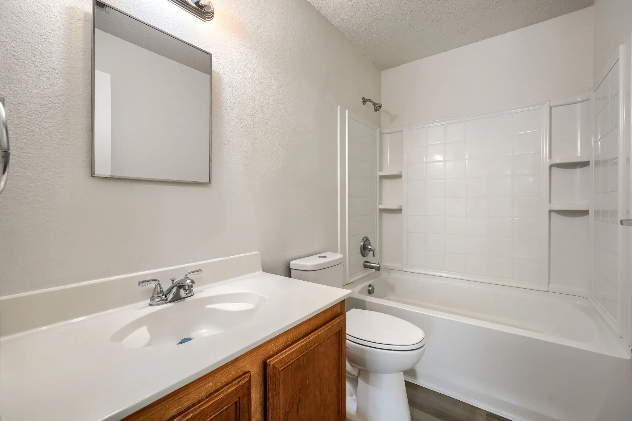 Bathroom featuring a wood-finish vanity, integrated sink, and a combination tub/shower with white tile surround