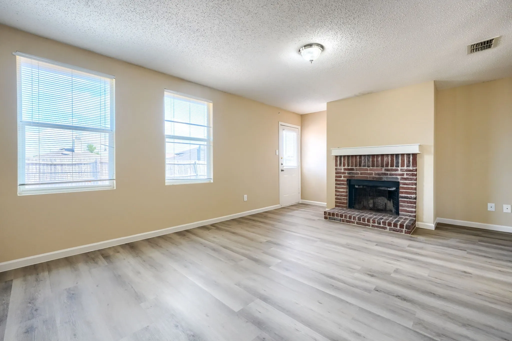 Living area featuring wood-finish flooring, a brick fireplace, two double-hung windows, and a ceiling-mounted light fixture