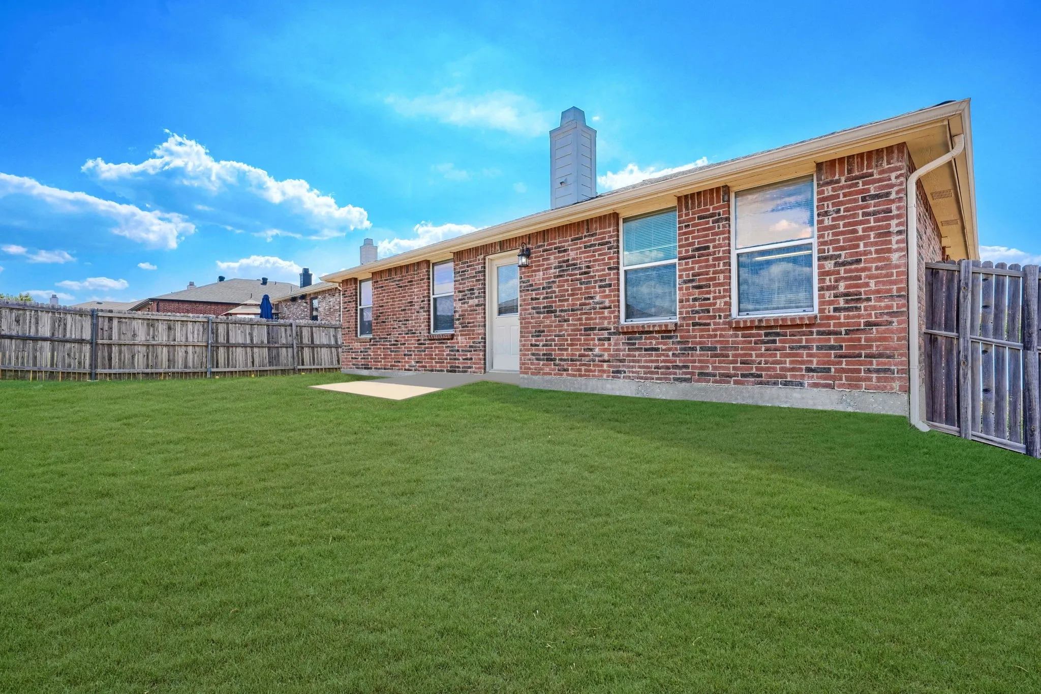 Expansive grassy yard with a concrete patio, wood privacy fencing, and brick exterior
