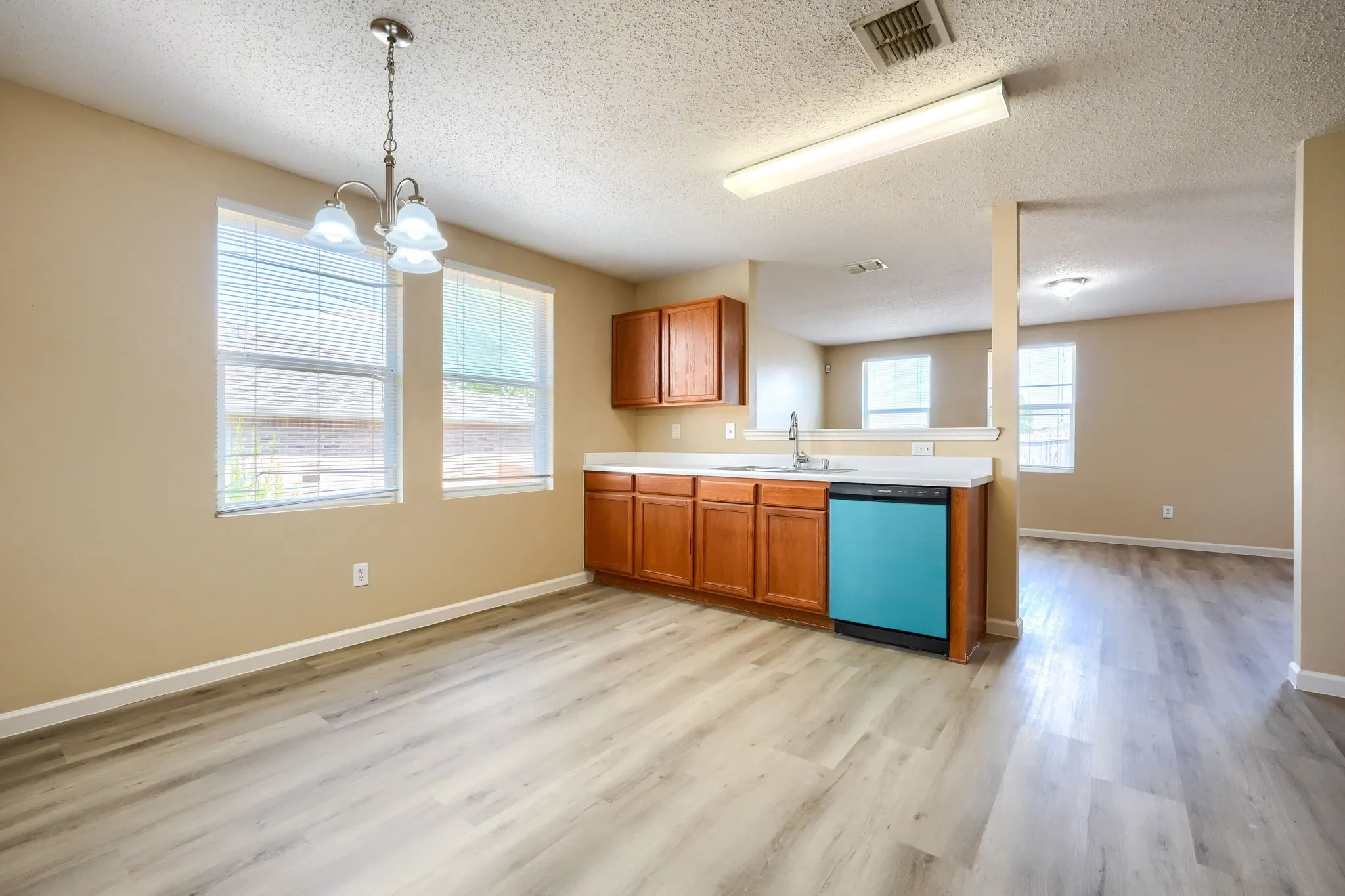 Dining area with wood-finish flooring, ample natural light through multiple windows, and a chandelier