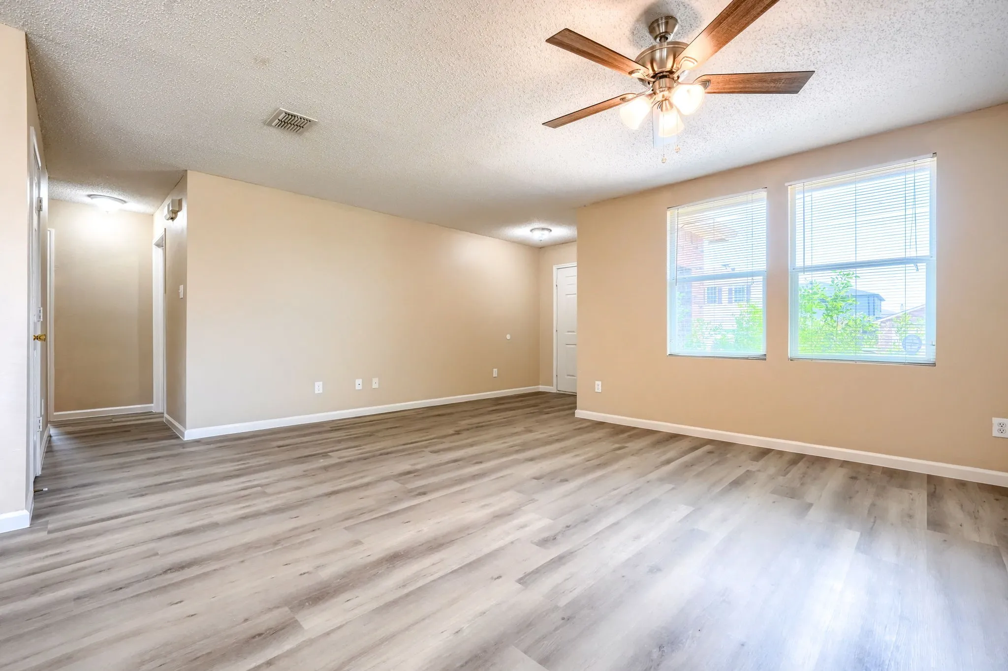 Spacious living area featuring wood-finish flooring, a ceiling fan with integrated lighting, and dual windows