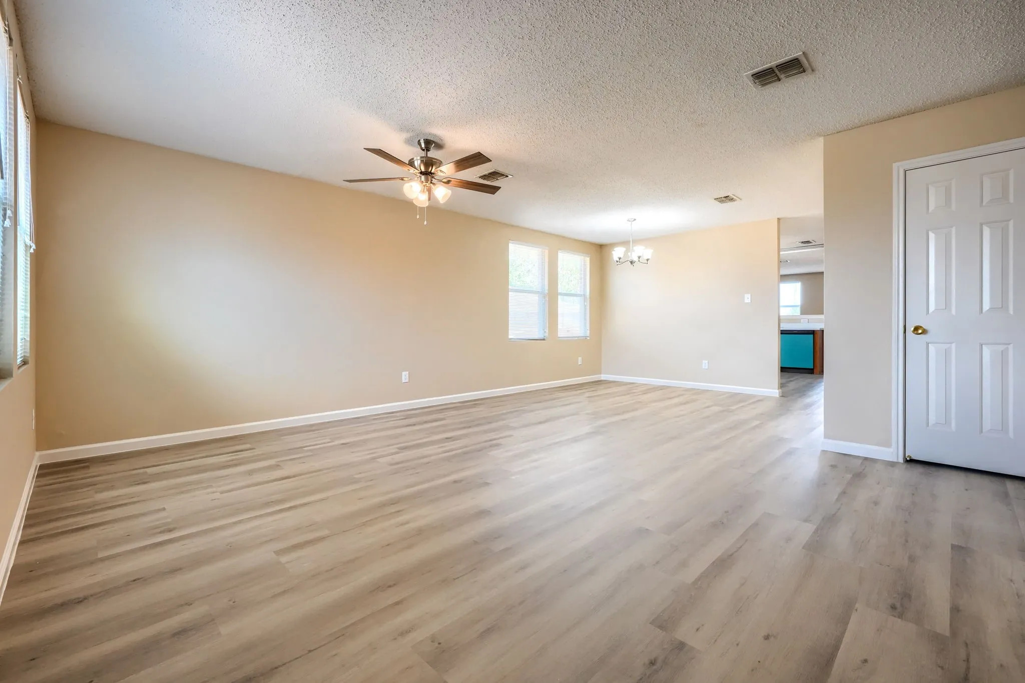 Spacious room featuring wood-finish flooring, neutral-toned walls, multiple windows, and a ceiling fan with integrated lighting