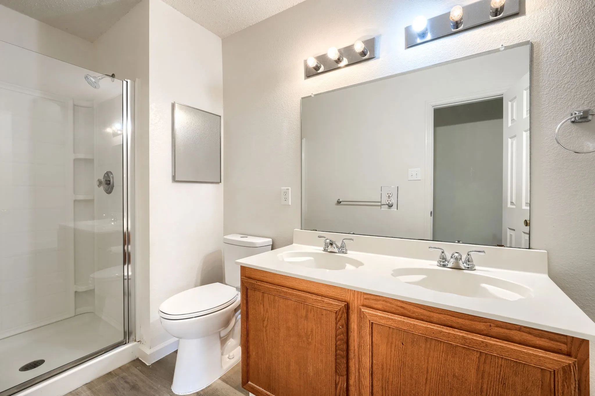 Dual vanity with integrated sinks, wood-finish cabinetry, frameless mirror, and a glass-enclosed shower
