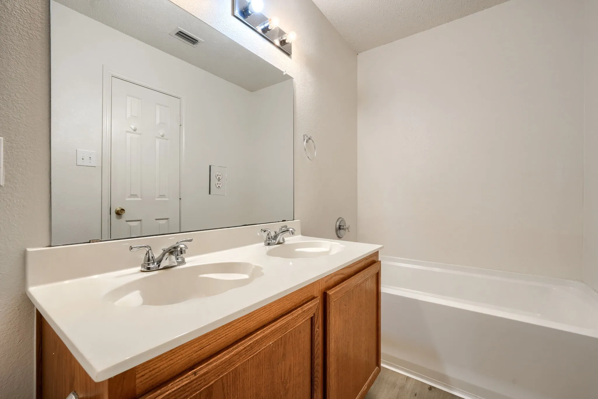 Dual vanity with integrated sinks, wood-finish cabinetry, full-width mirror, and a built-in bathtub