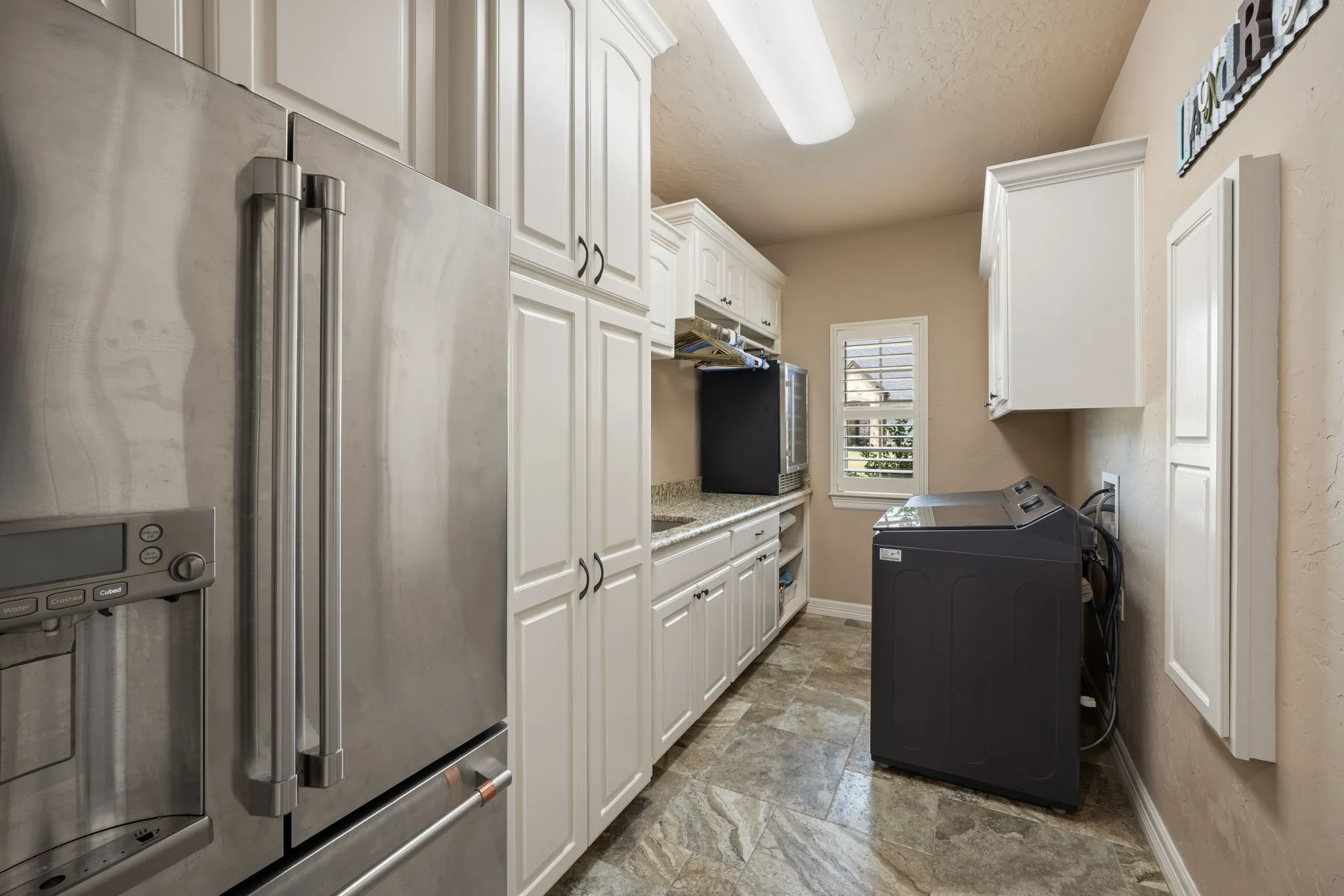 Modern galley kitchen featuring stainless steel appliances, white shaker-style cabinetry with chrome hardware, quartz countertops, and tile flooring