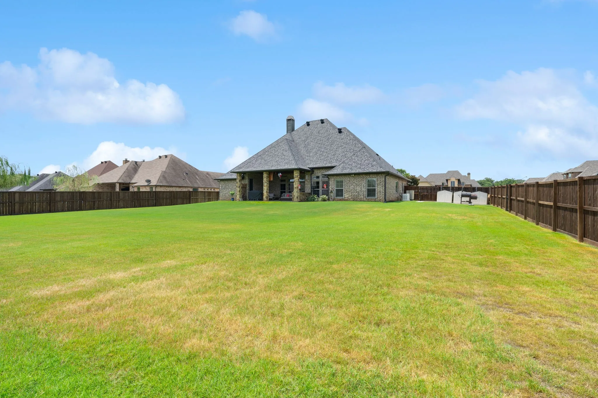 Expansive backyard featuring a manicured lawn, full privacy fencing, and stone exterior with a covered patio